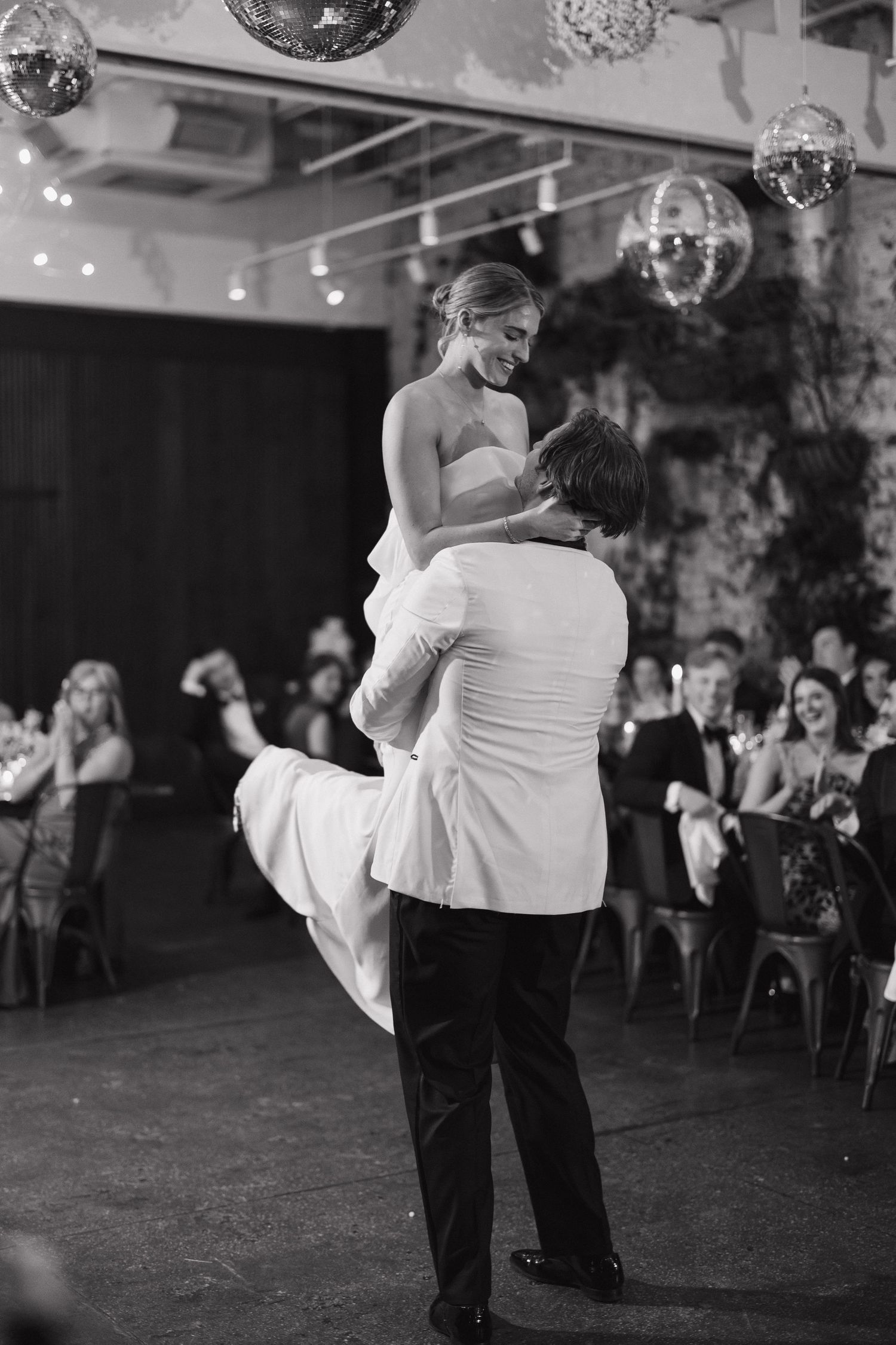Black and white photo of a wedding dance under disco balls in an industrial venue.