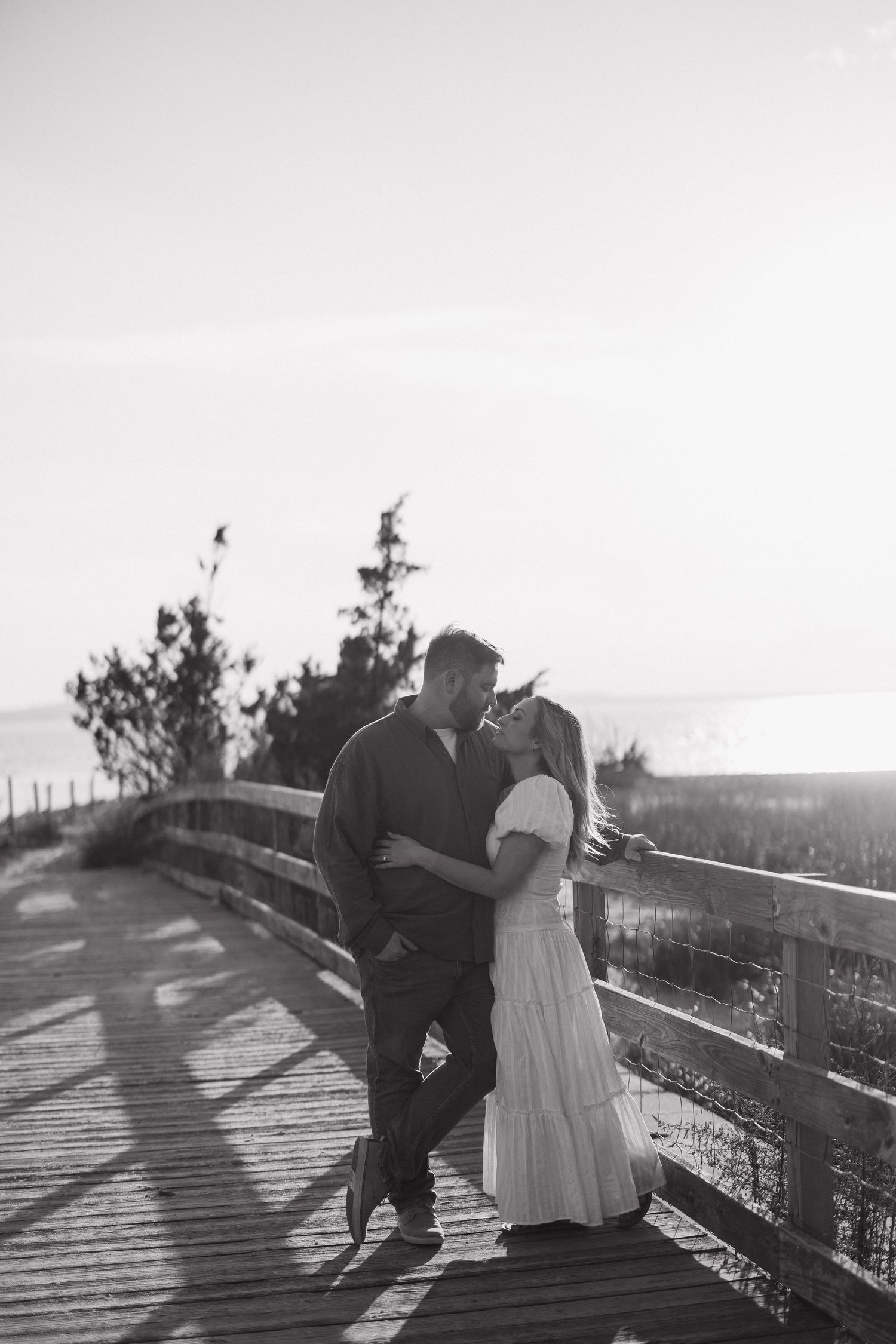 Black and white photos of a couple posing together on a wooden boardwalk at sunset.