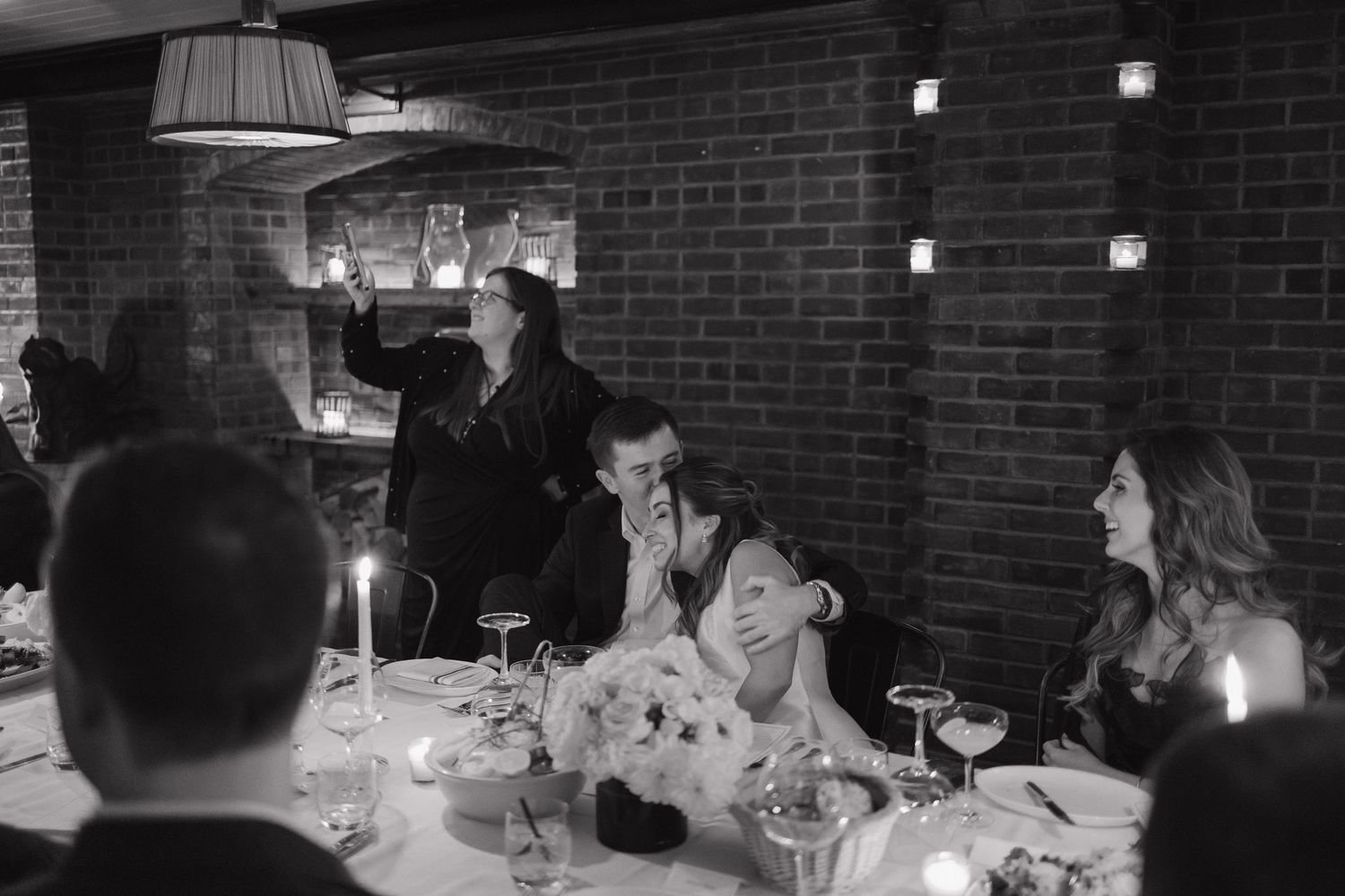 Black and white candid photo of wedding reception dinner with guests at candlelit table.