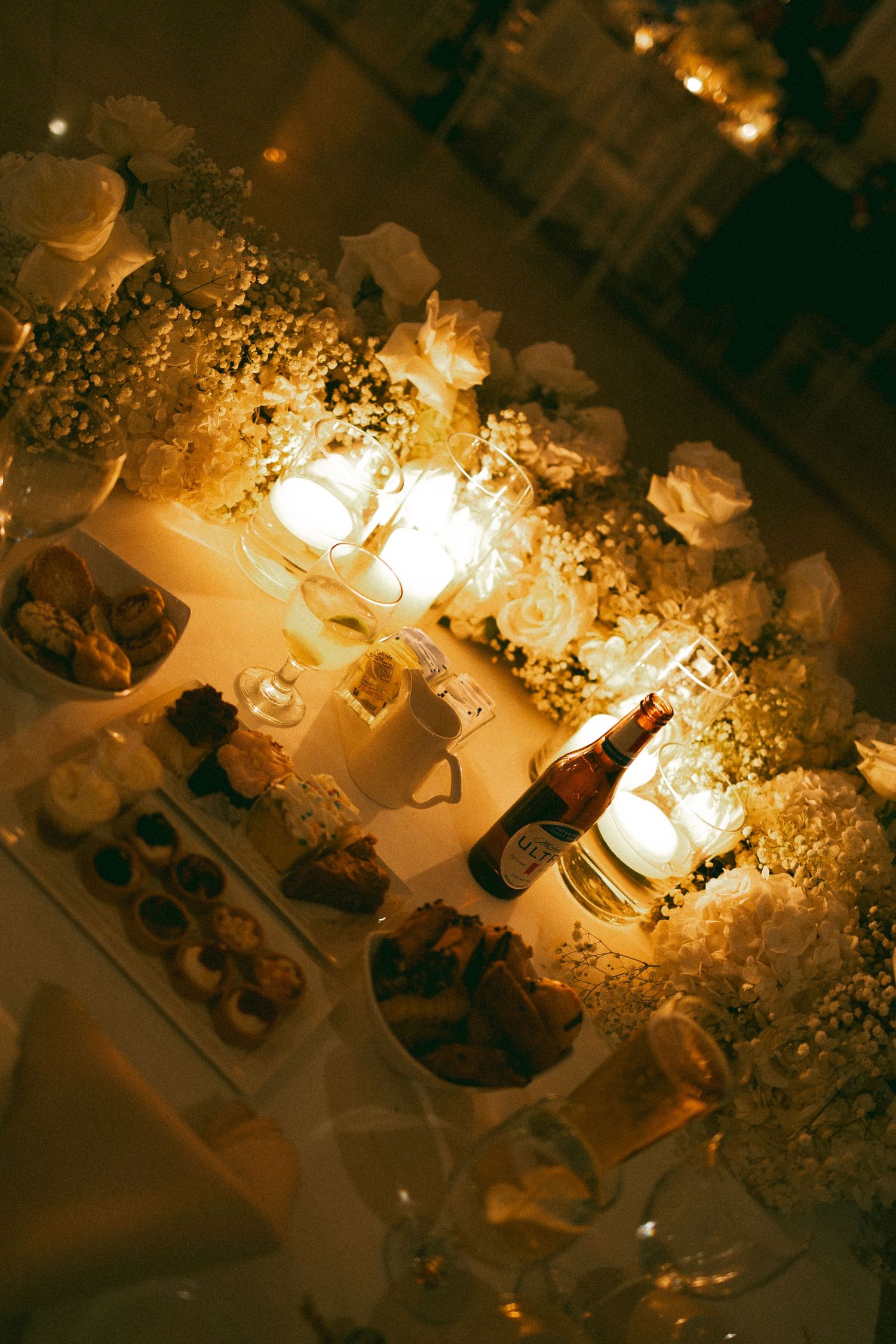 Candlelit table setting with desserts and treats creates a warm, romantic ambiance at an evening gathering.