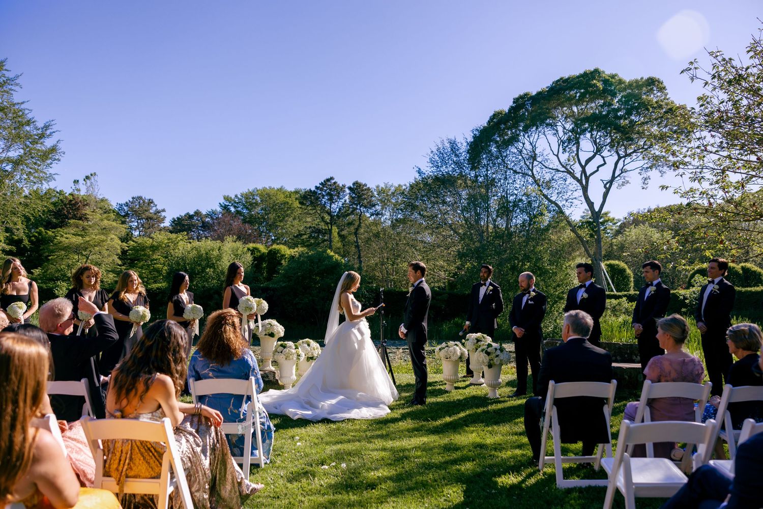 Panoramic view of an outdoor wedding ceremony with guests seated in rows on a lawn.