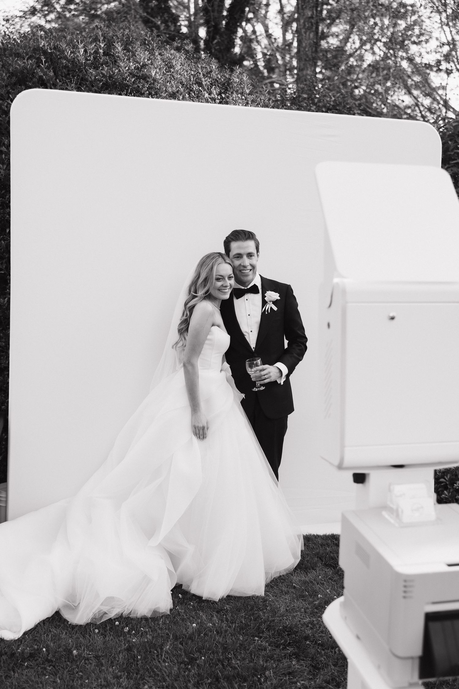 Wedding couple poses creatively with a white grand piano outdoors on grass.