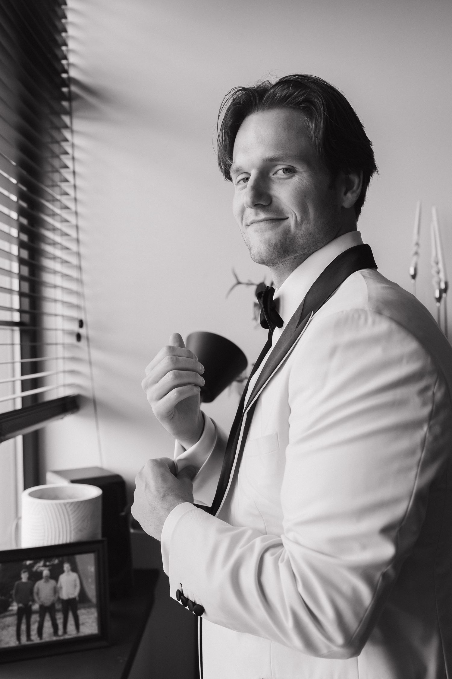 Black and white photo of someone in formal attire holding a coffee cup near a window.