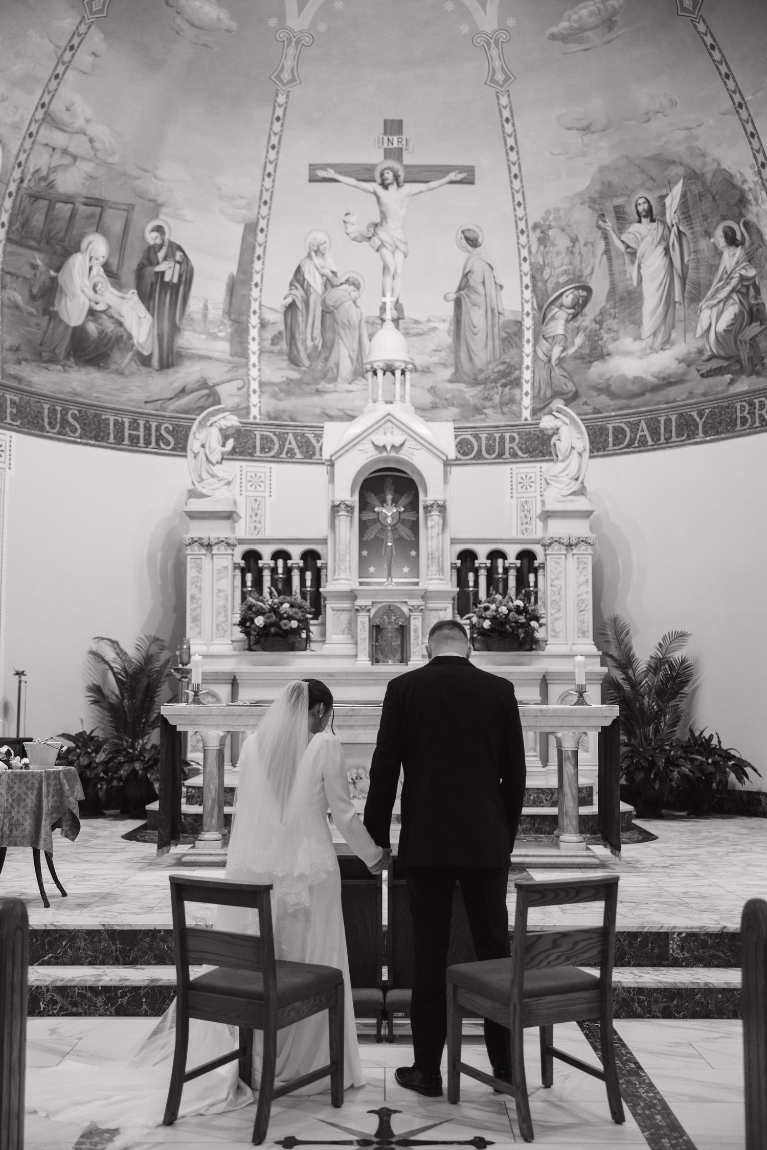 Black and white wedding ceremony in a church sanctuary with ornate religious murals and decorations.