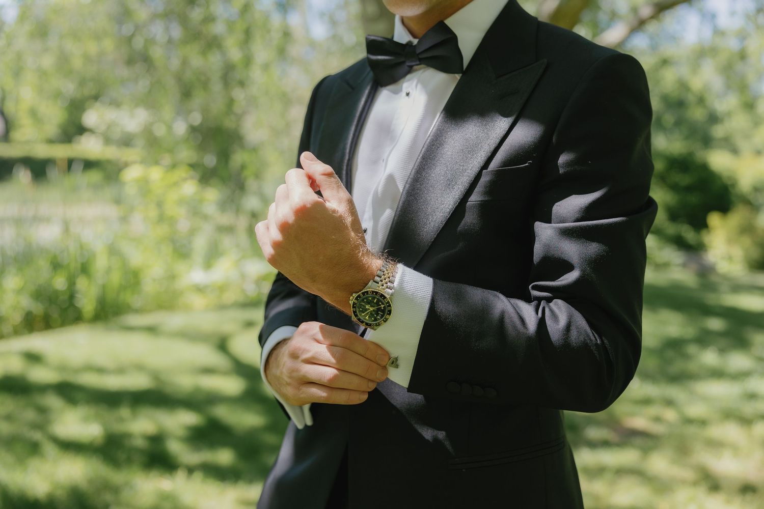 Close-up shots of a person in a black suit adjusting cufflinks and tie while standing outdoors in natural lighting.