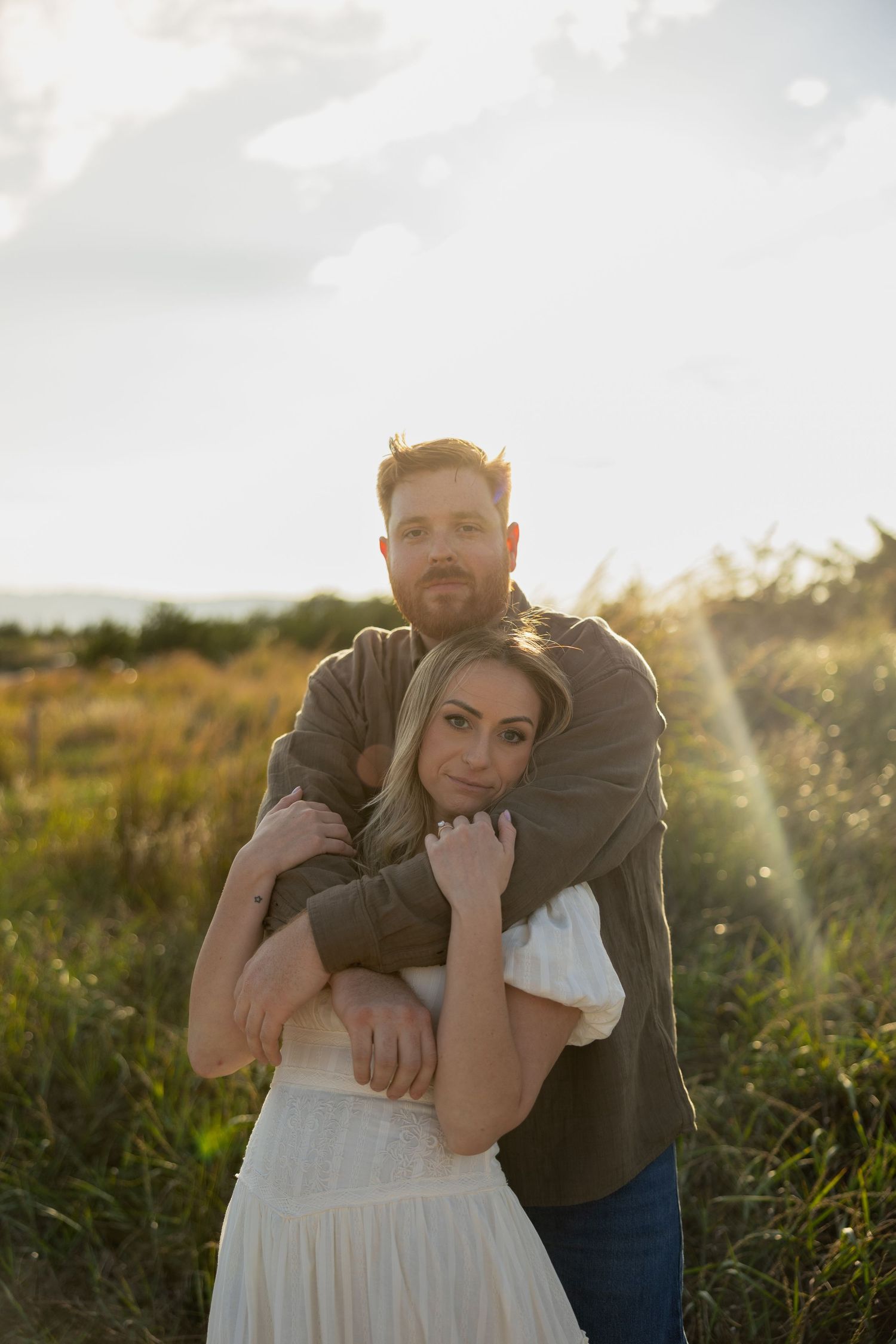 Romantic sunset engagement photos show couple embracing in golden field of wildflowers.