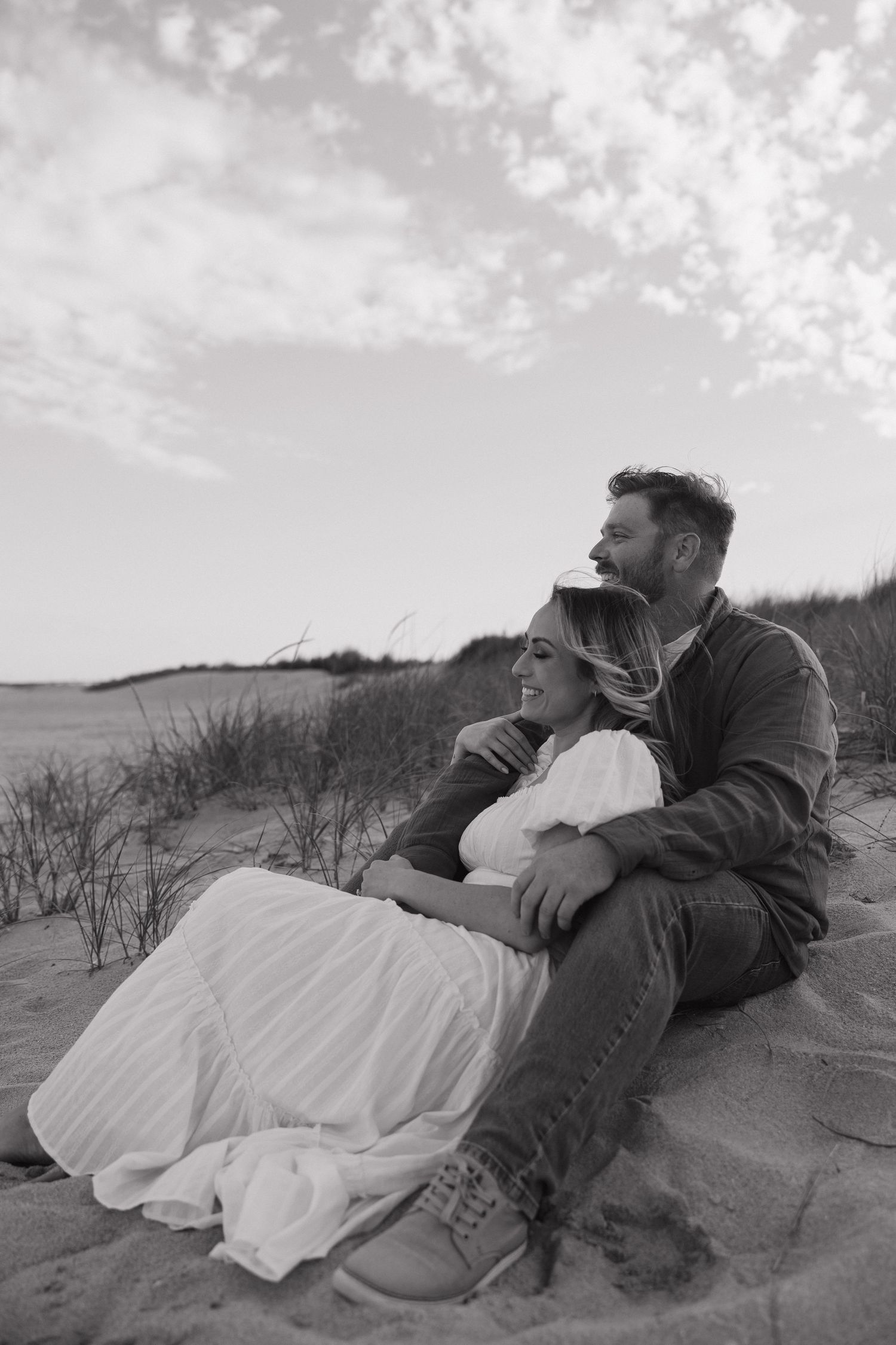 Couple lying together on sandy dunes during a romantic photoshoot at sunset.