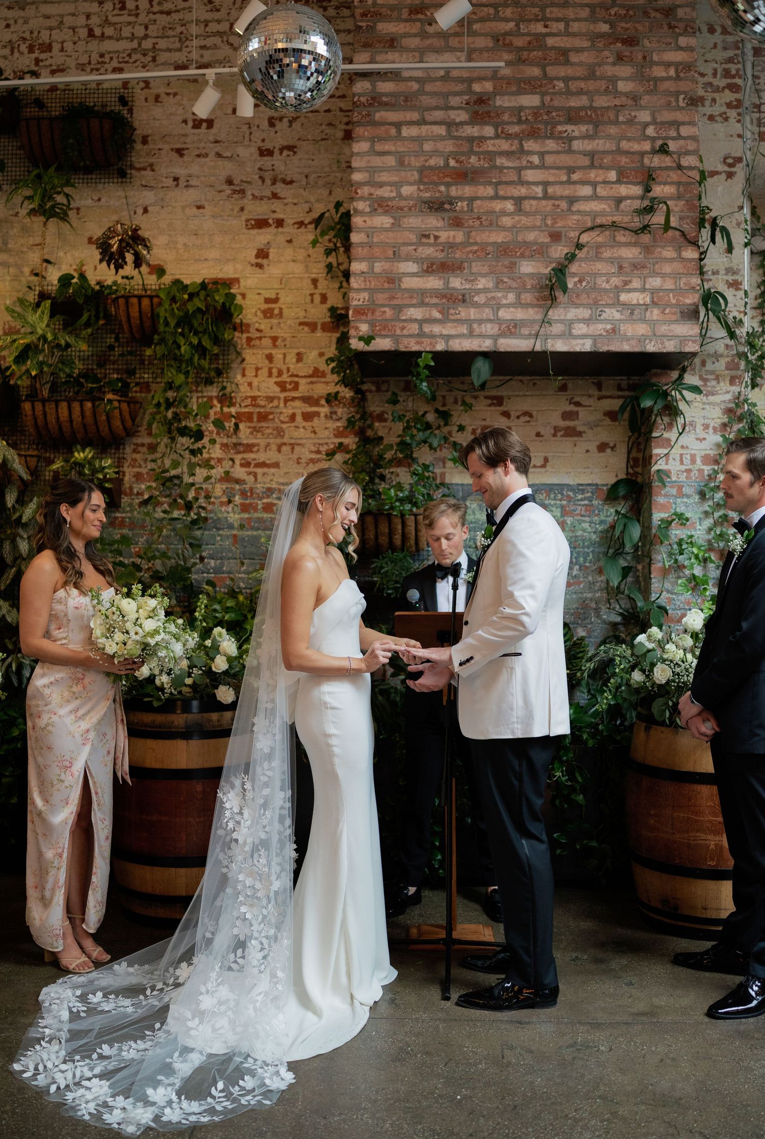 Wedding ceremony in rustic brick venue with disco ball and greenery decorations.