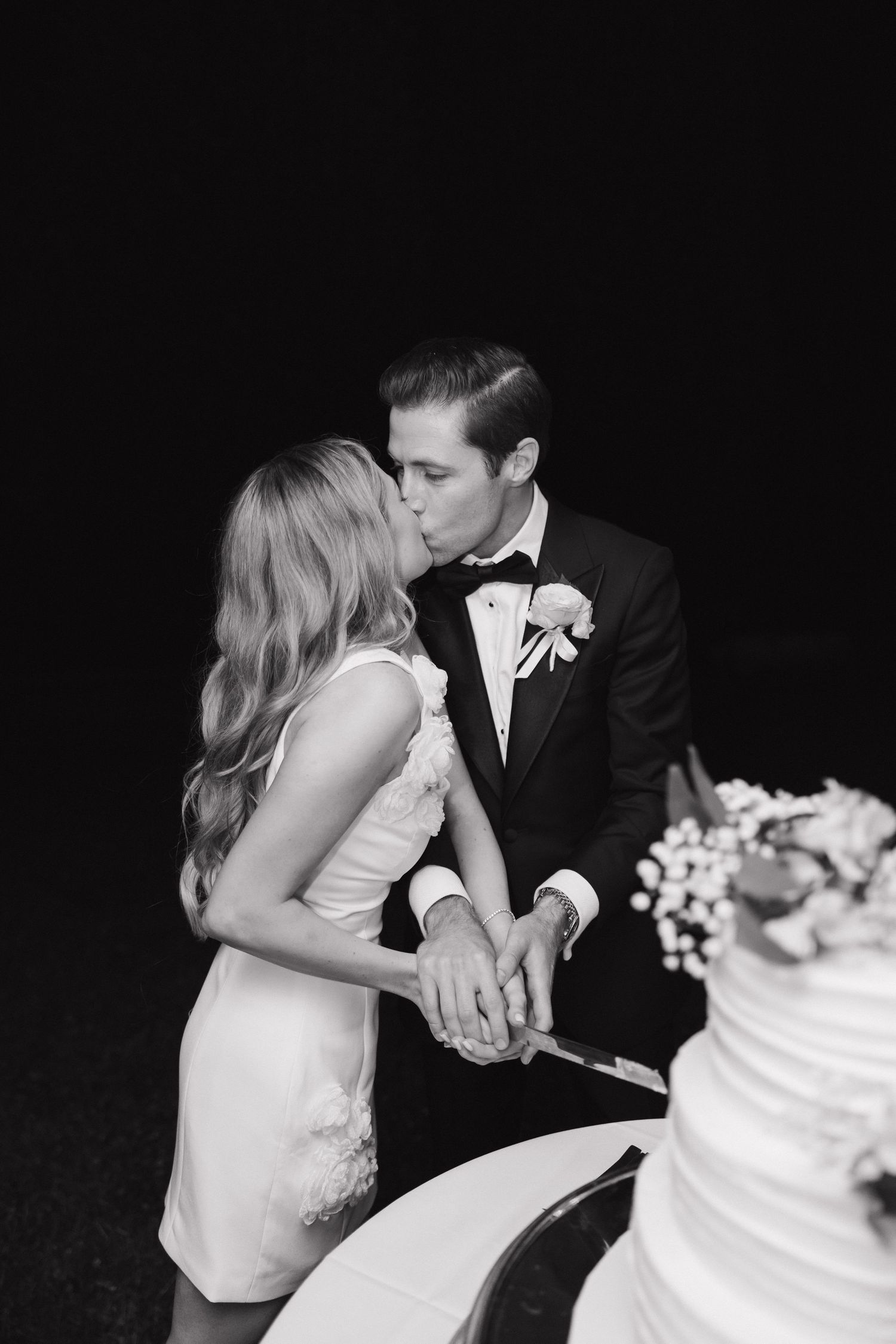 Romantic black and white photo of a couple cutting their tiered wedding cake.