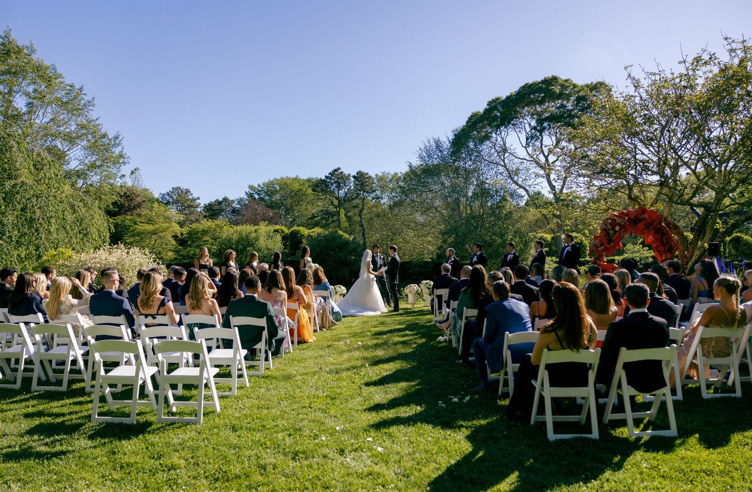 Panoramic view of outdoor wedding ceremony seating arranged on a grassy hillside under blue skies.