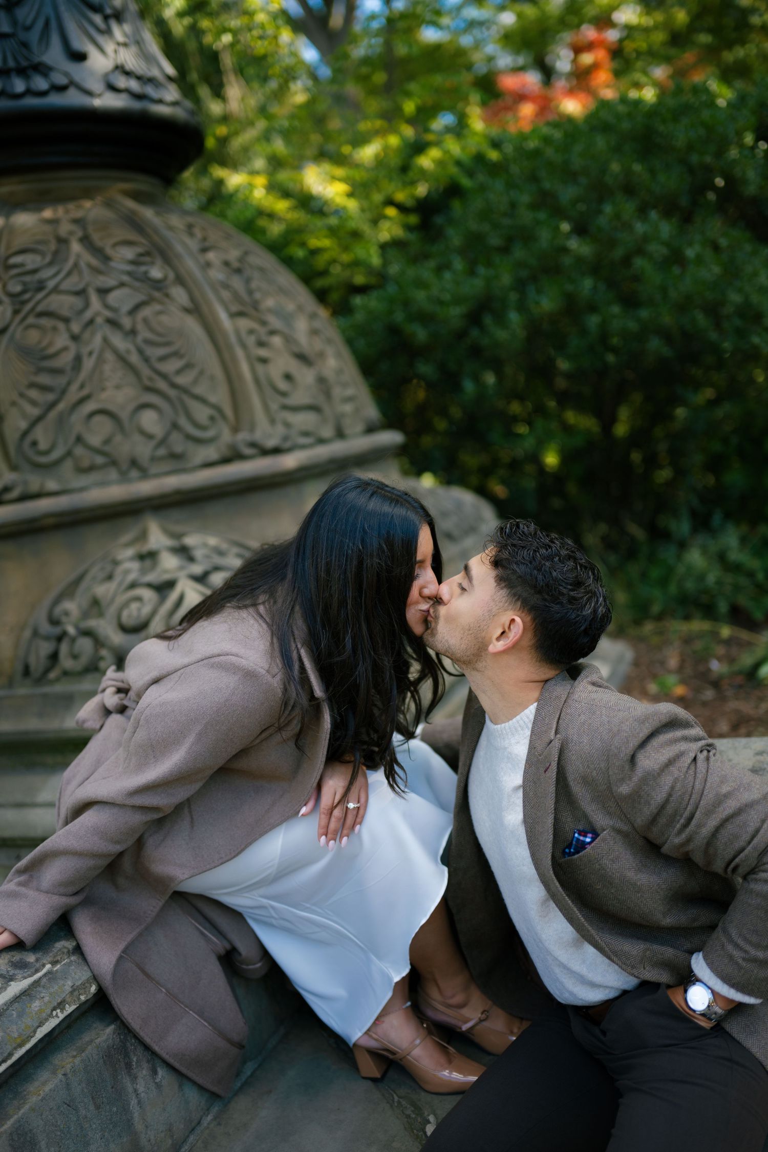 Romantic moment captured on decorative stone steps surrounded by autumn trees.