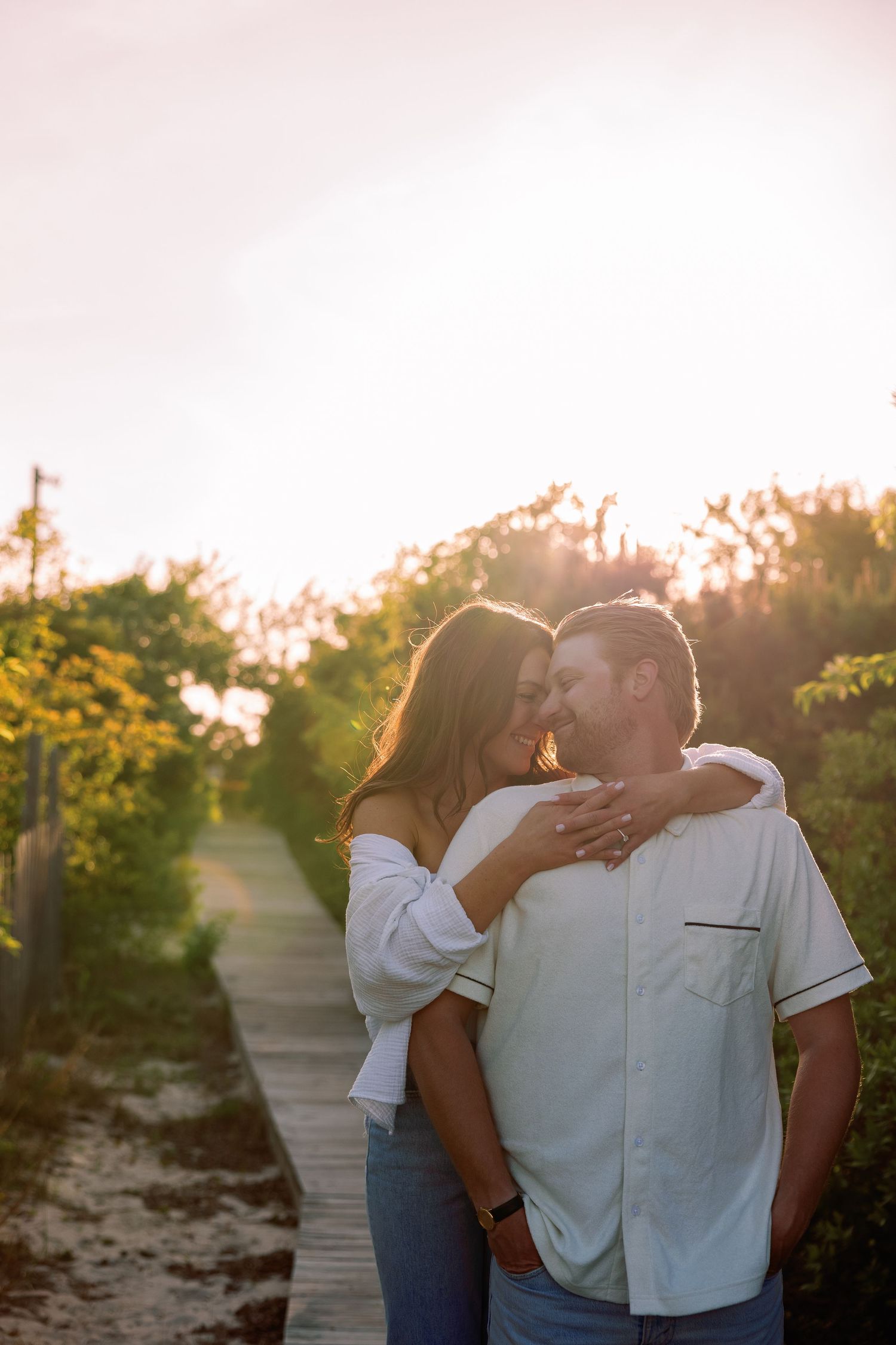 Intimate sunset engagement photo of couple embracing on a wooden boardwalk.