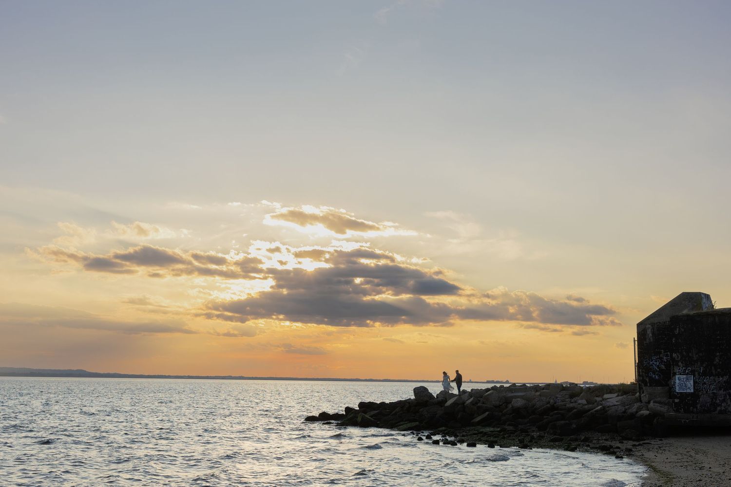 Scenic sunset over the ocean with silhouettes on a rocky shoreline and colorful clouds.