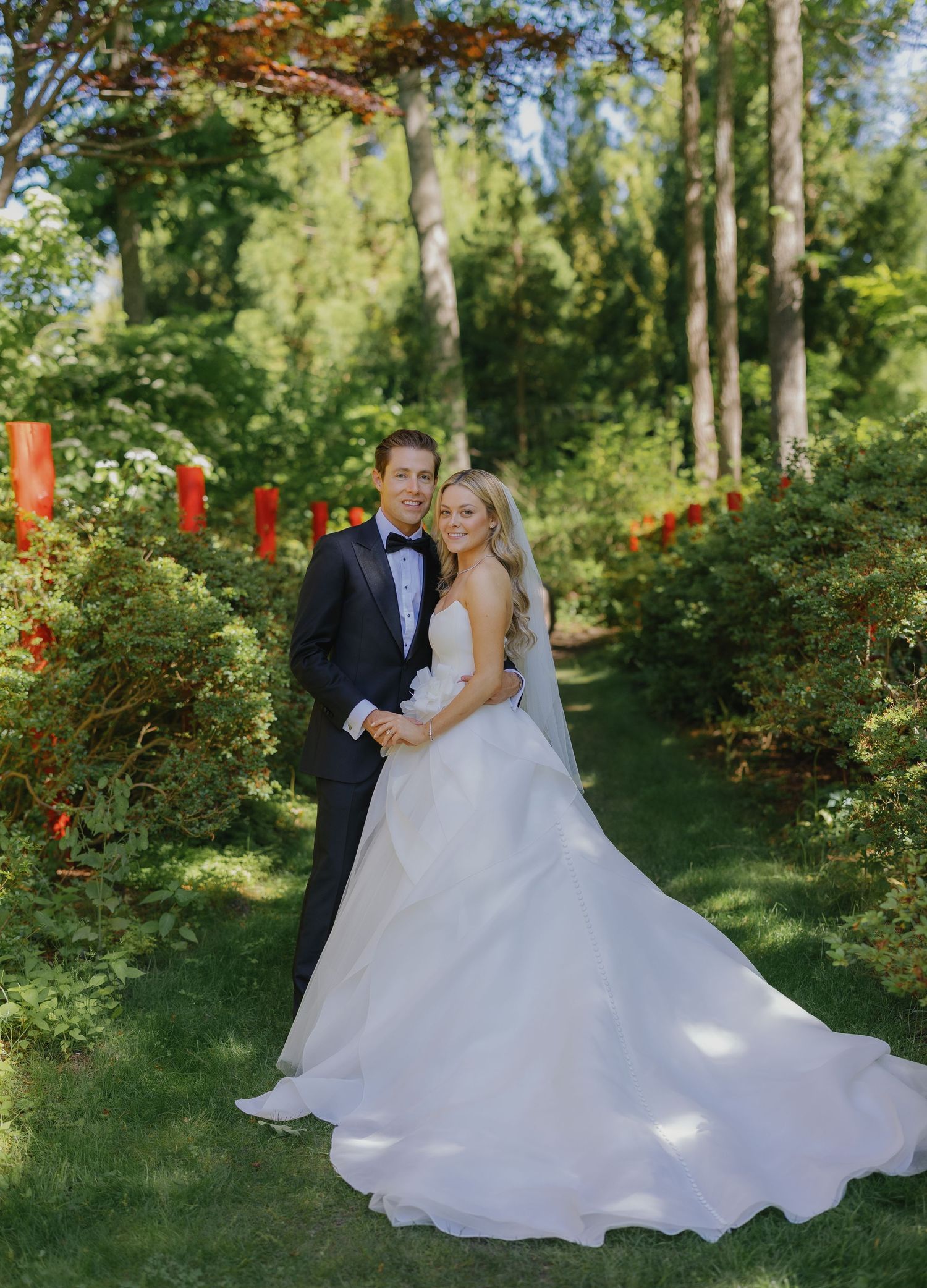 Wedding couple posing for romantic photos in a garden setting with red flowers.