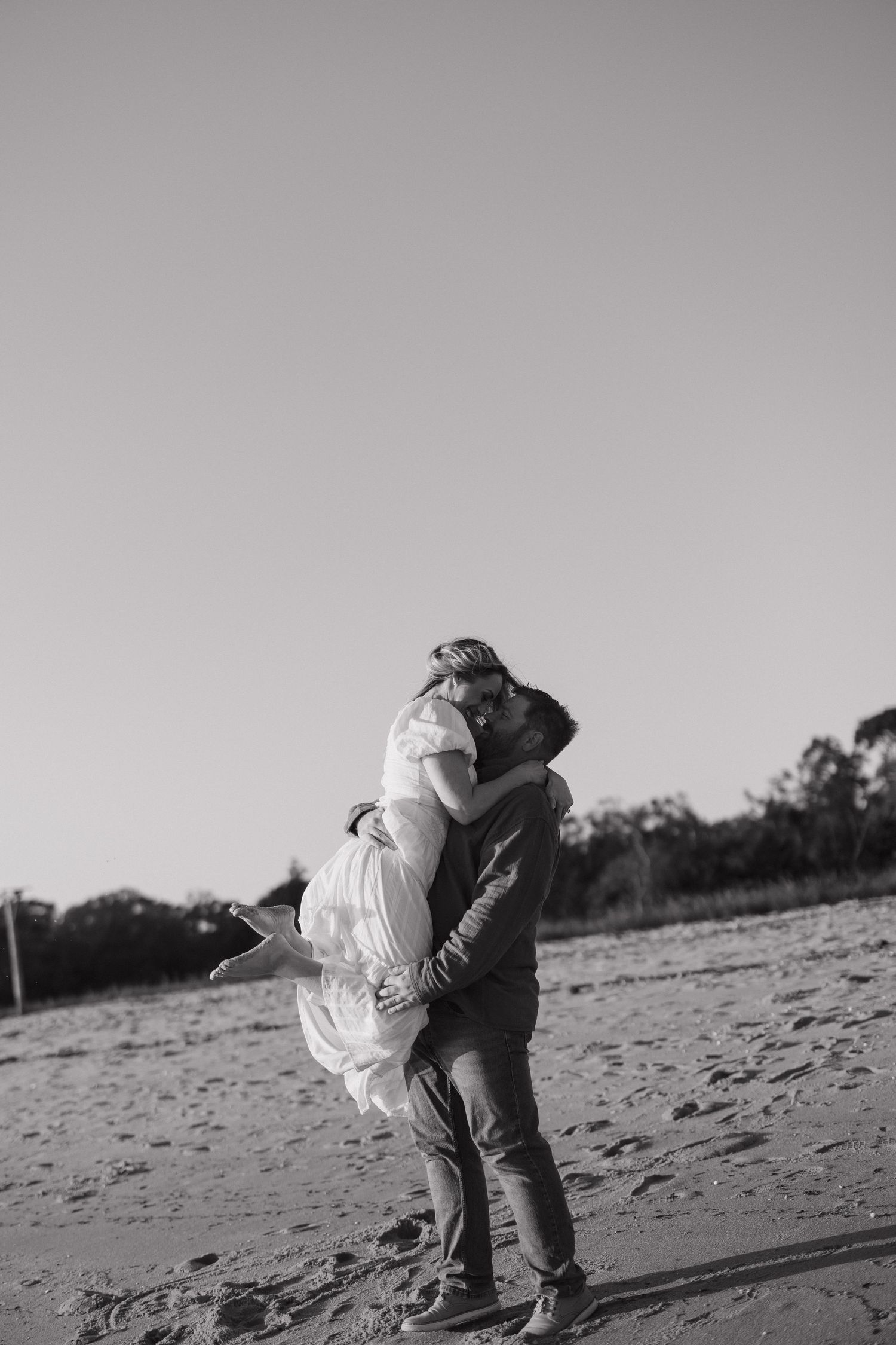 A sequence of black and white photos showing two people embracing on a sandy beach at sunset.