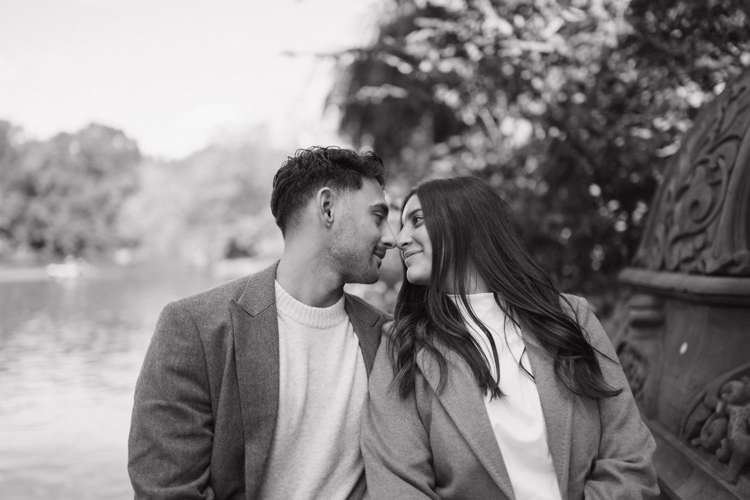 A romantic black and white portrait of a couple sharing an intimate moment by a lake with mountains in the background.