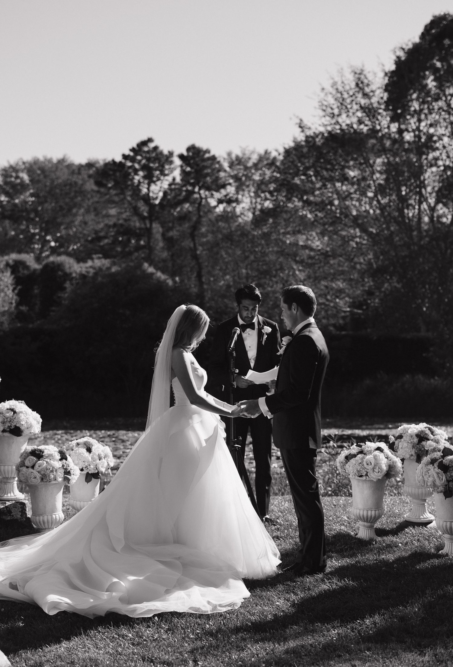 Black and white photo of a wedding ceremony in a garden setting with flowing white dress.