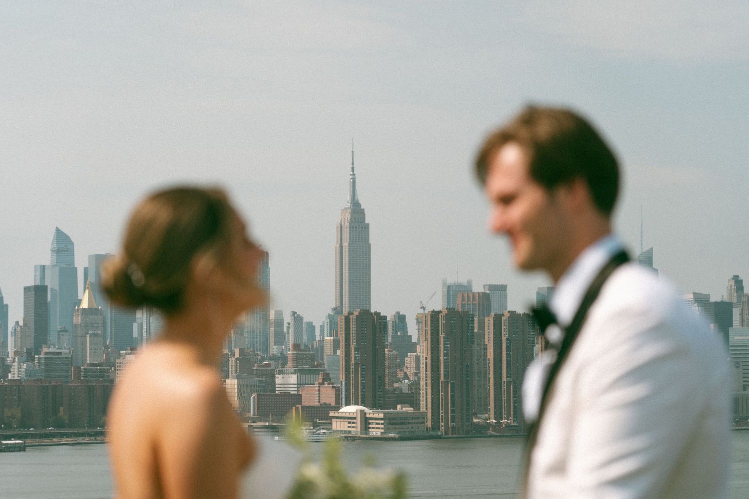 Stylish couple poses on rooftop with Empire State Building in background.