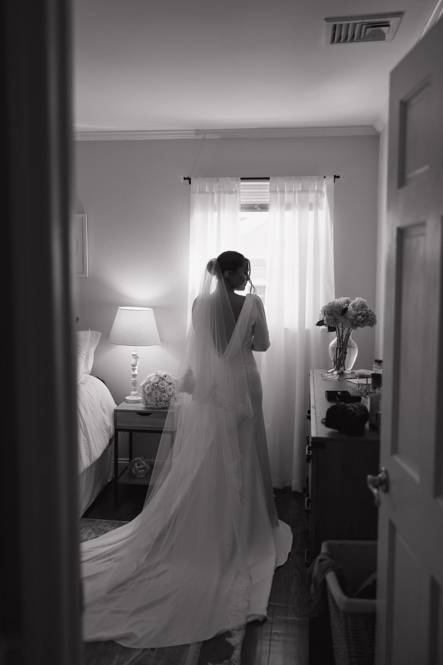 A black and white series showing a flowing wedding dress and veil silhouetted against bright windows in a room.