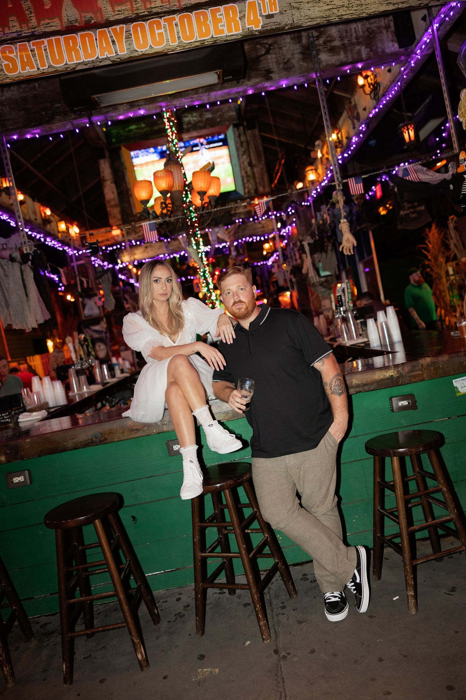 Couple dancing and embracing at a festive bar decorated with purple string lights.