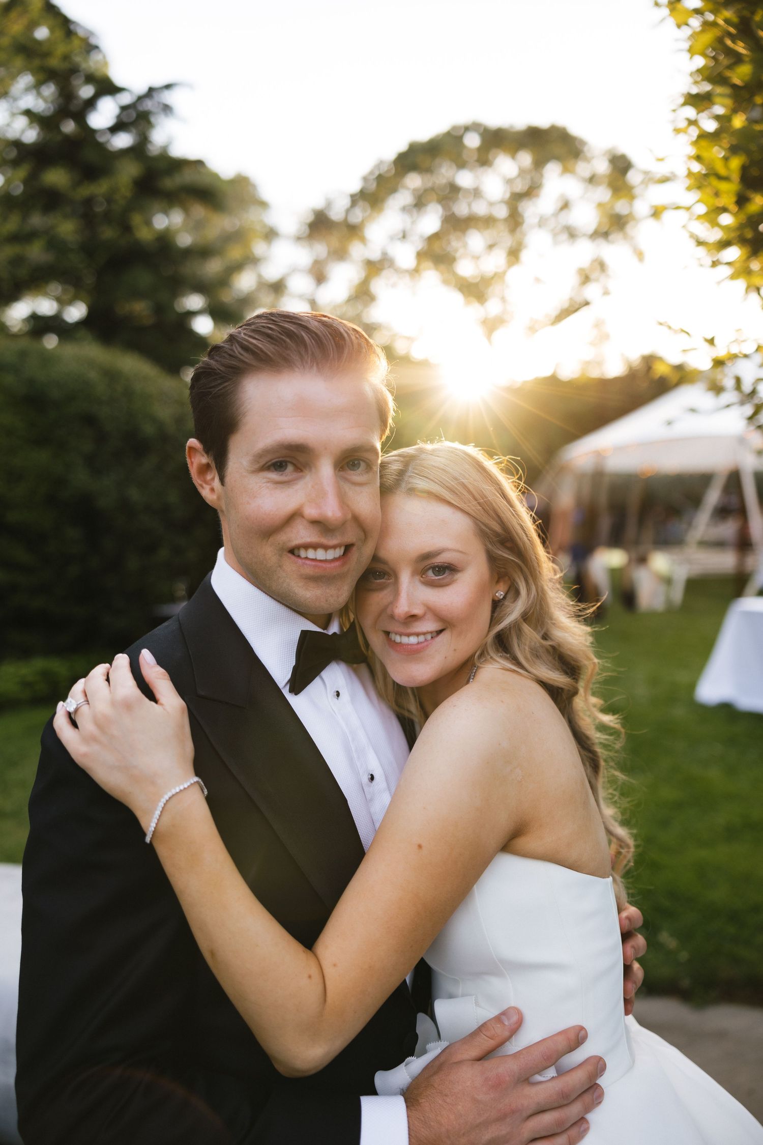 A couple embraces outdoors during sunset in wedding attire at their romantic garden ceremony.
