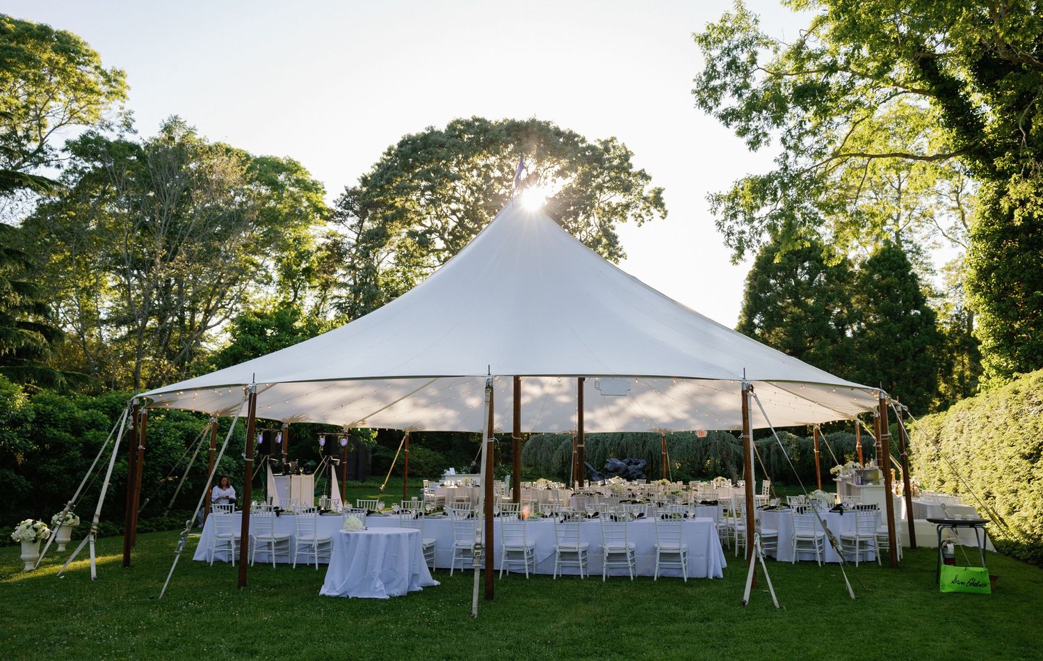 Large white wedding reception tents set up on a green lawn surrounded by trees.