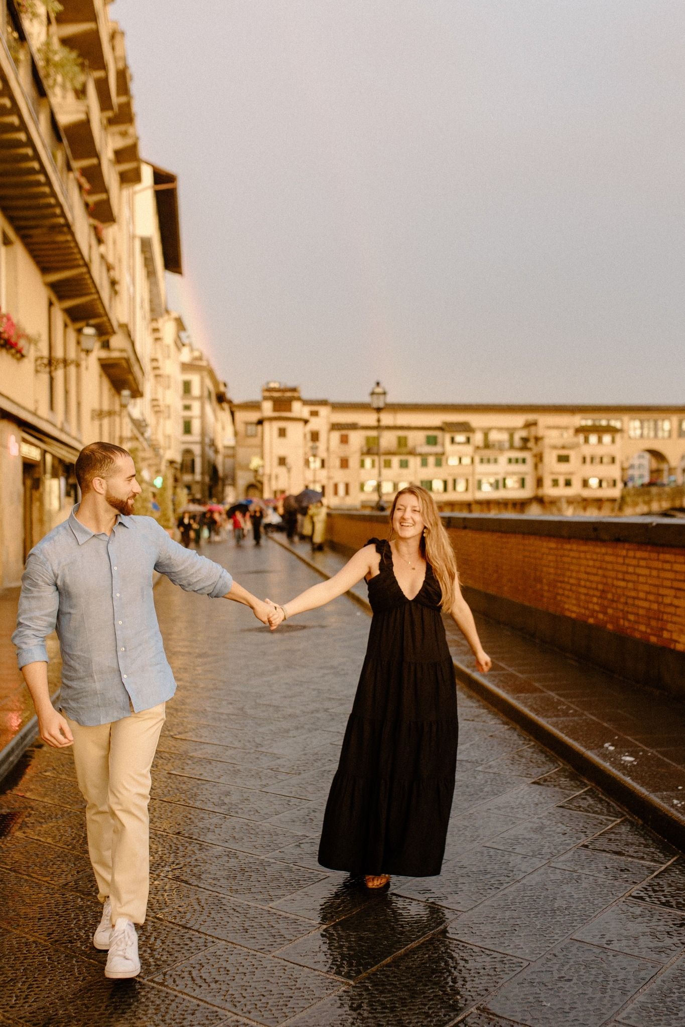 Couple walking along historic Ponte Vecchio bridge in Florence during sunset.