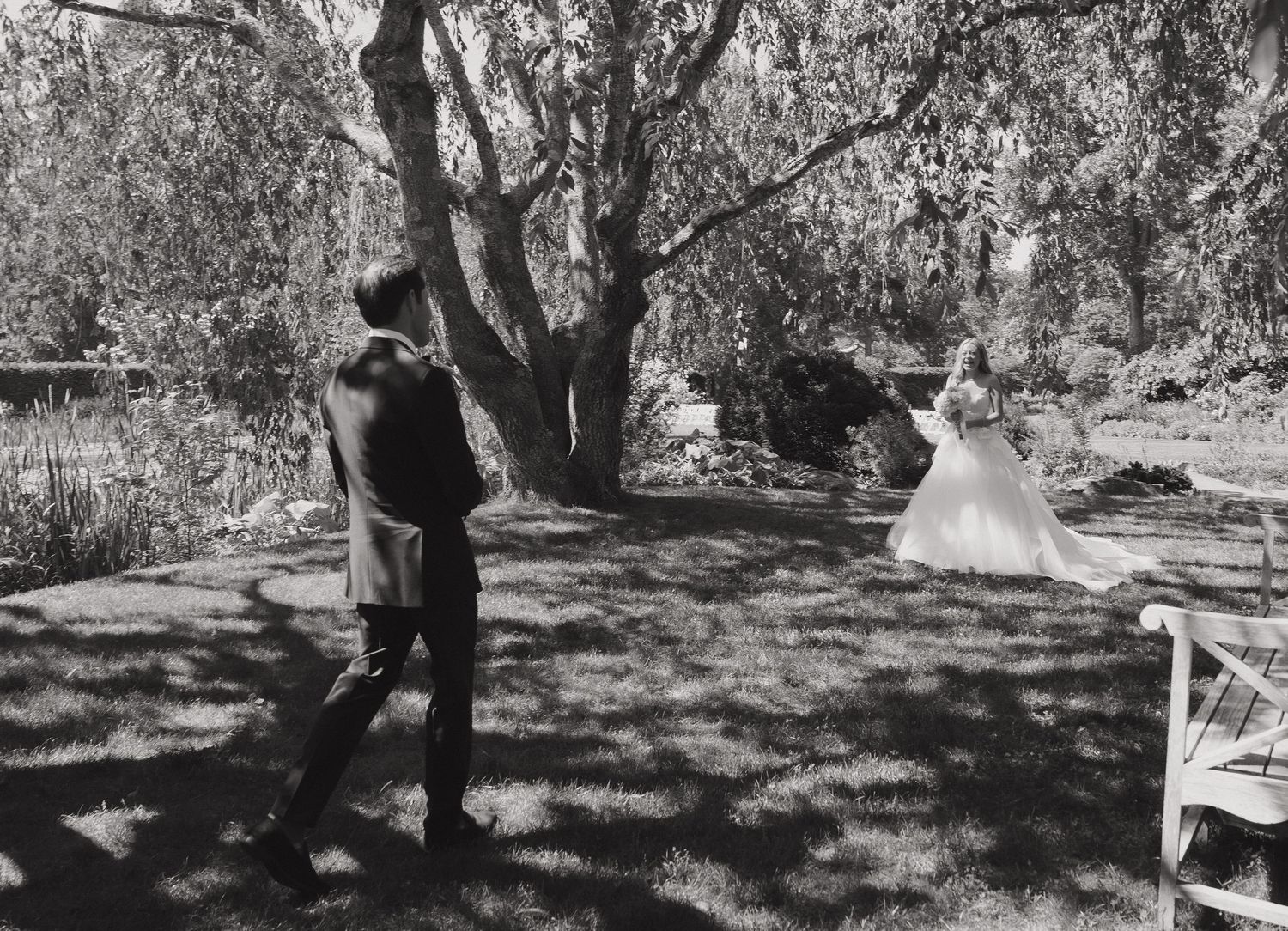 Black and white photo of a wedding ceremony taking place under trees in a garden setting.