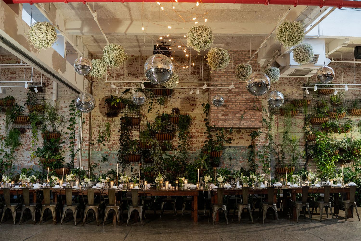 Rustic wedding reception venue decorated with twinkling lights, disco balls, and greenery hanging from exposed brick walls.
