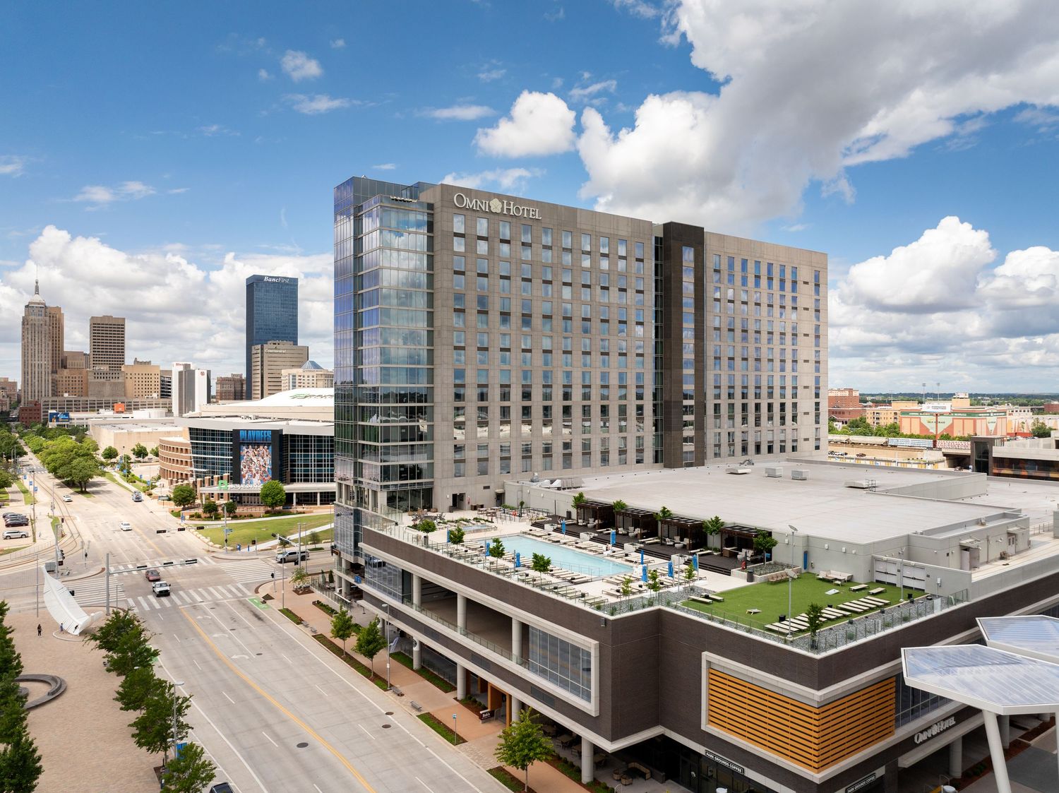 Modern medical center building with rooftop garden terrace and glass facade under blue cloudy sky in urban setting.