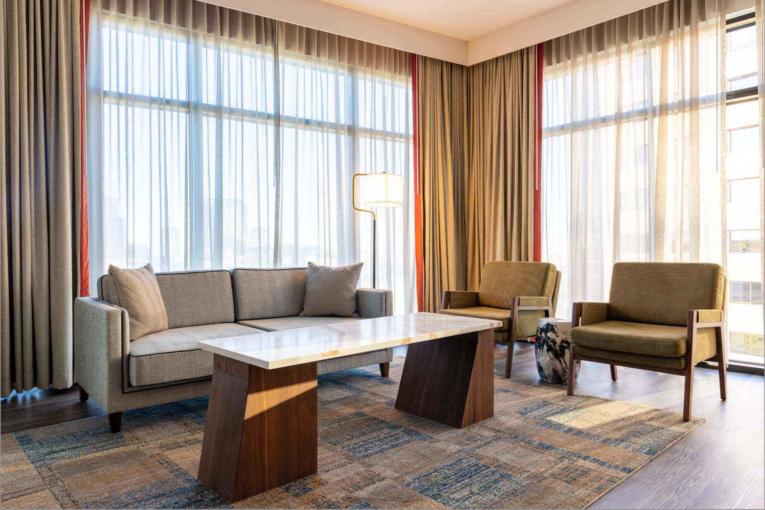 Modern living room interior with grey sofa, brown armchairs and wood coffee tables on patterned area rug.