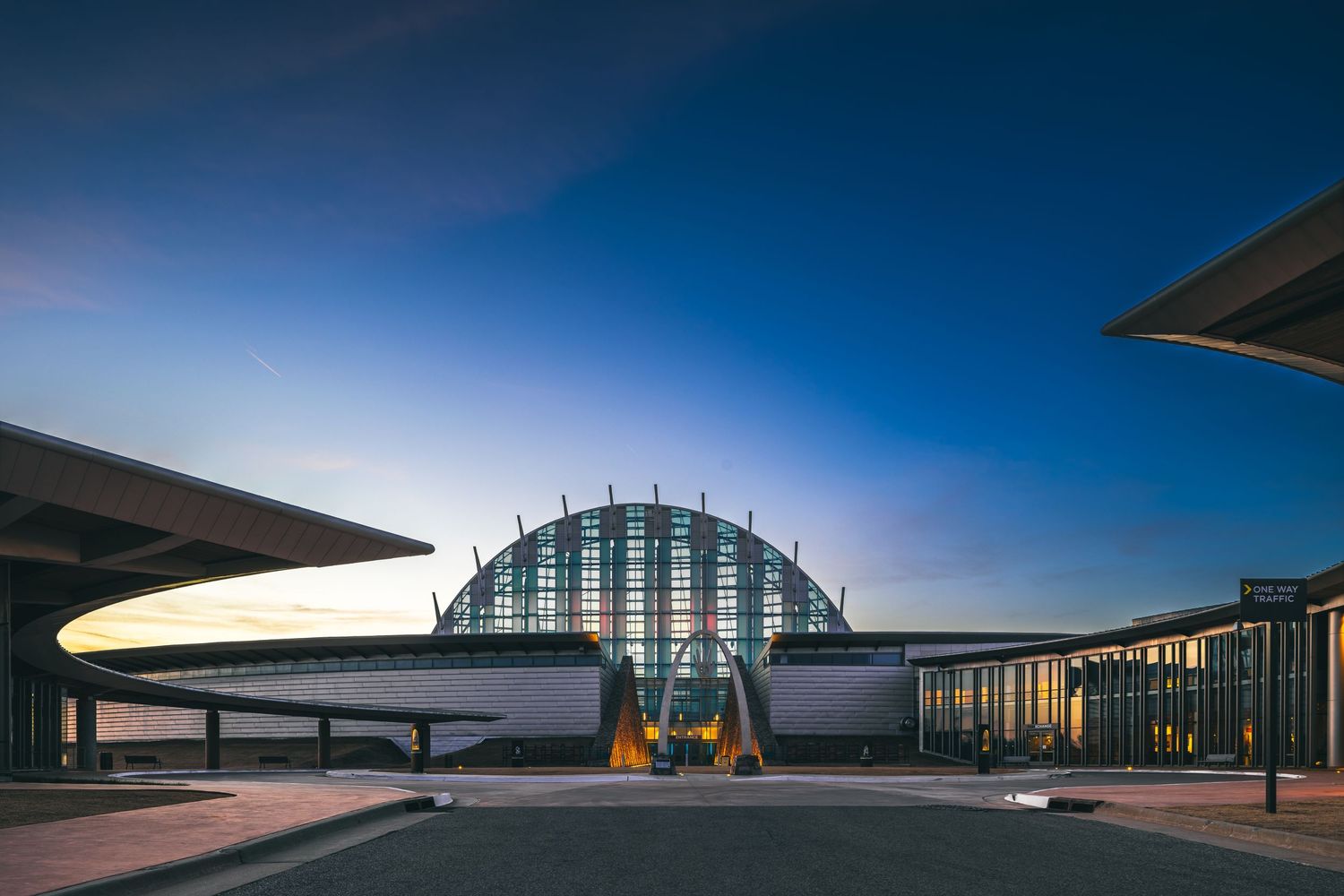 Modern architectural exterior of transportation terminal with domed glass roof and curved design elements at dusk.