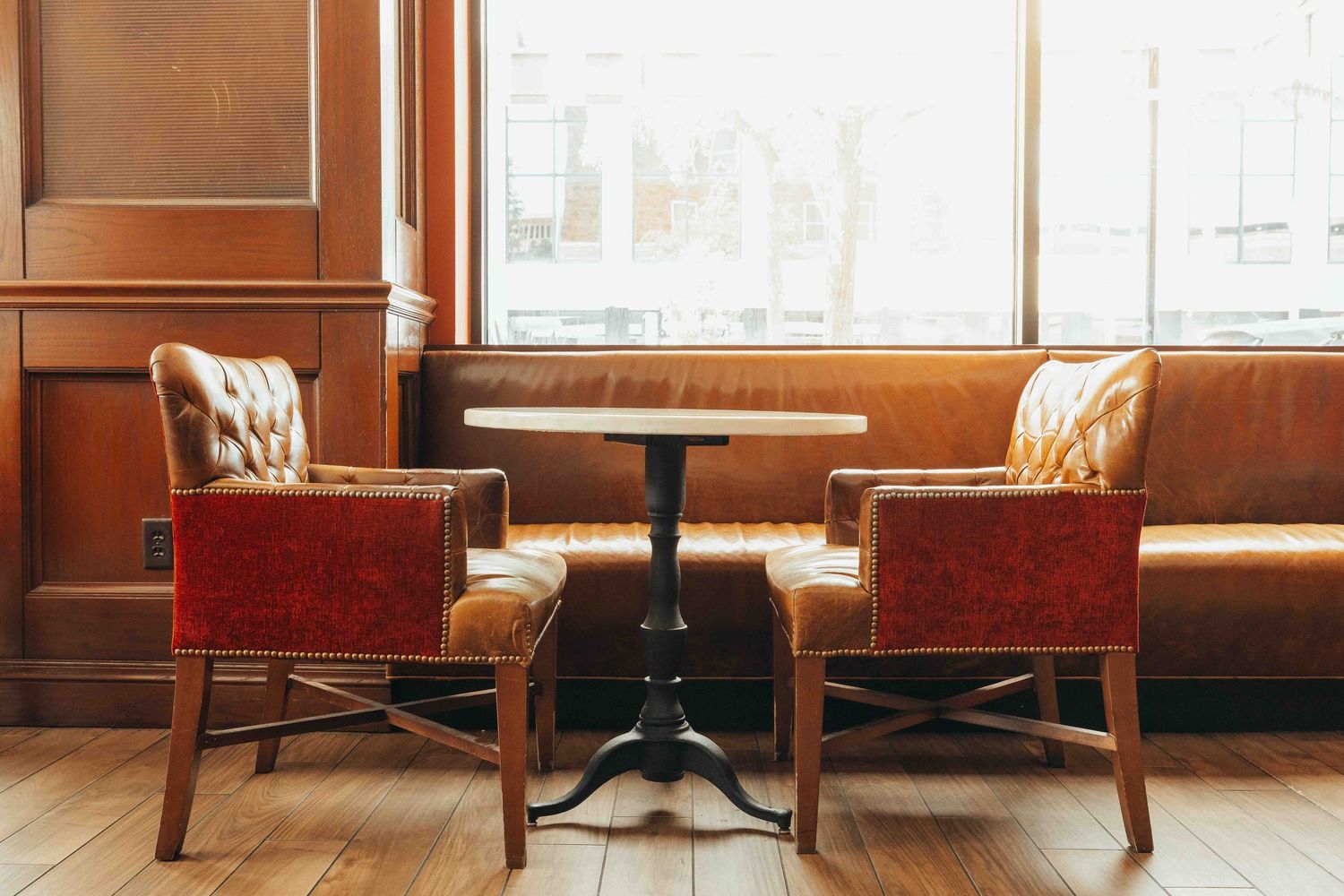 Empty vintage diner booth with red upholstered chairs and wooden table next to large window in warm lighting.