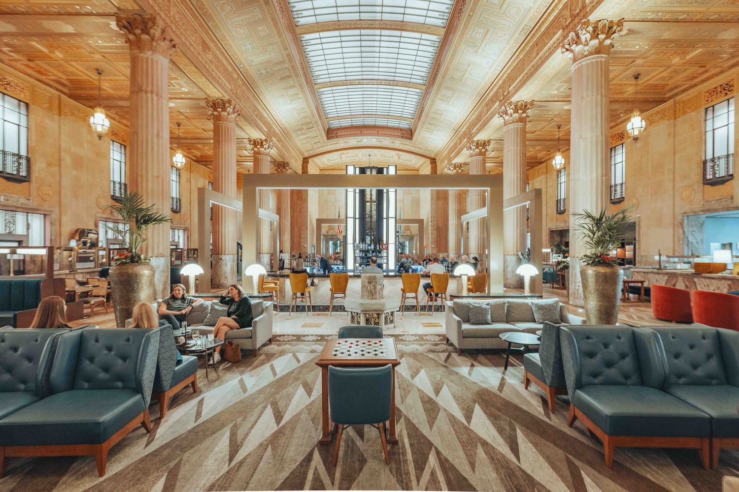 Elegant hotel lobby interior with skylight, marble columns, plush seating, and geometric patterns in warm lighting.
