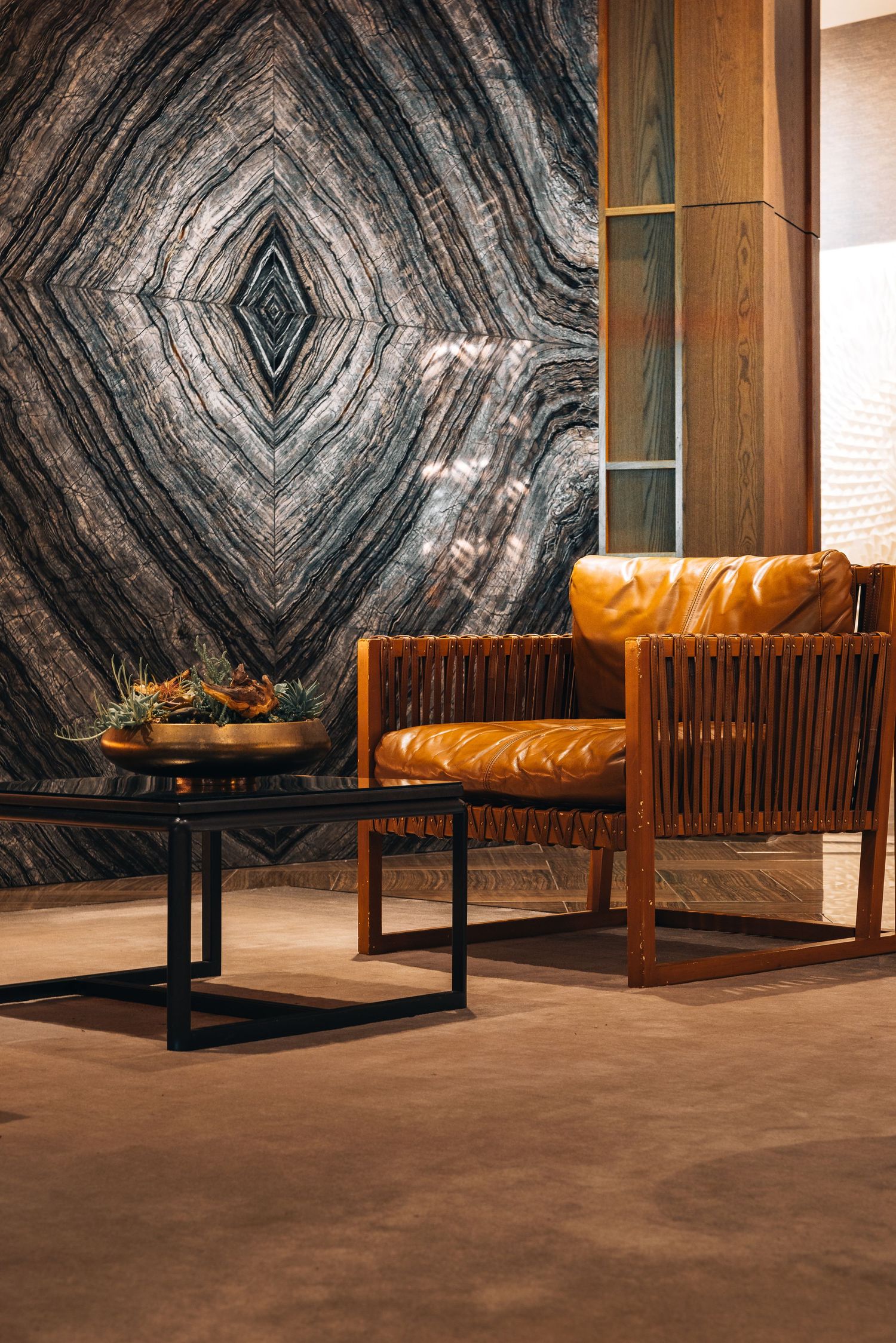 Luxurious seating area featuring dramatic diamond-patterned marble wall and cognac leather chair.
