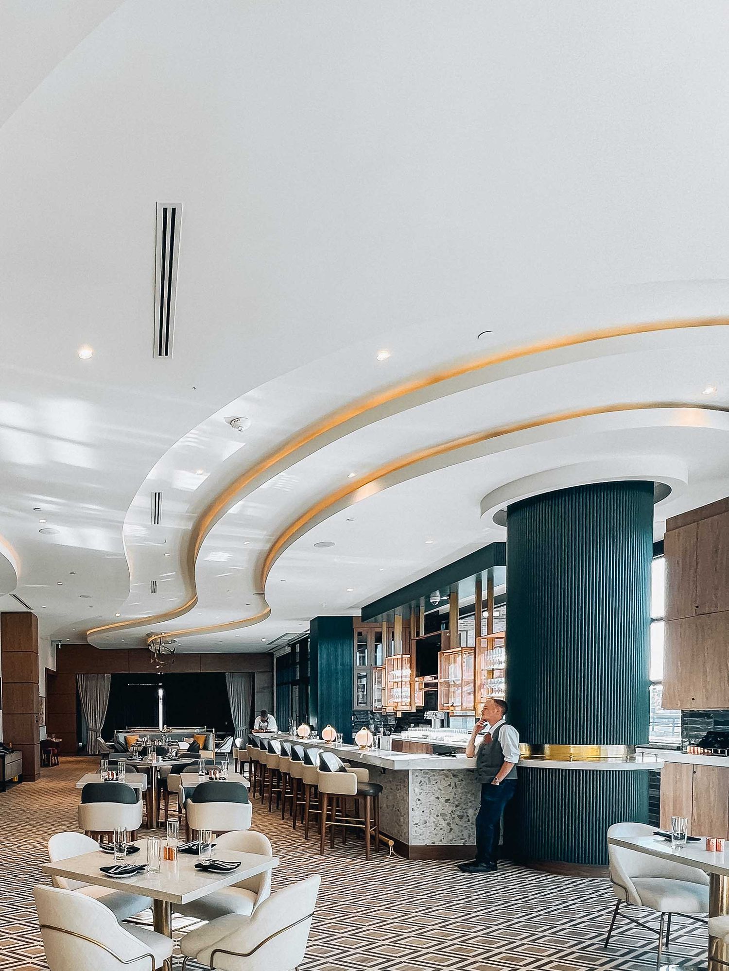Modern luxury restaurant interior with curved ceiling details, teal columns, and bar seating in an elegant dining space.
