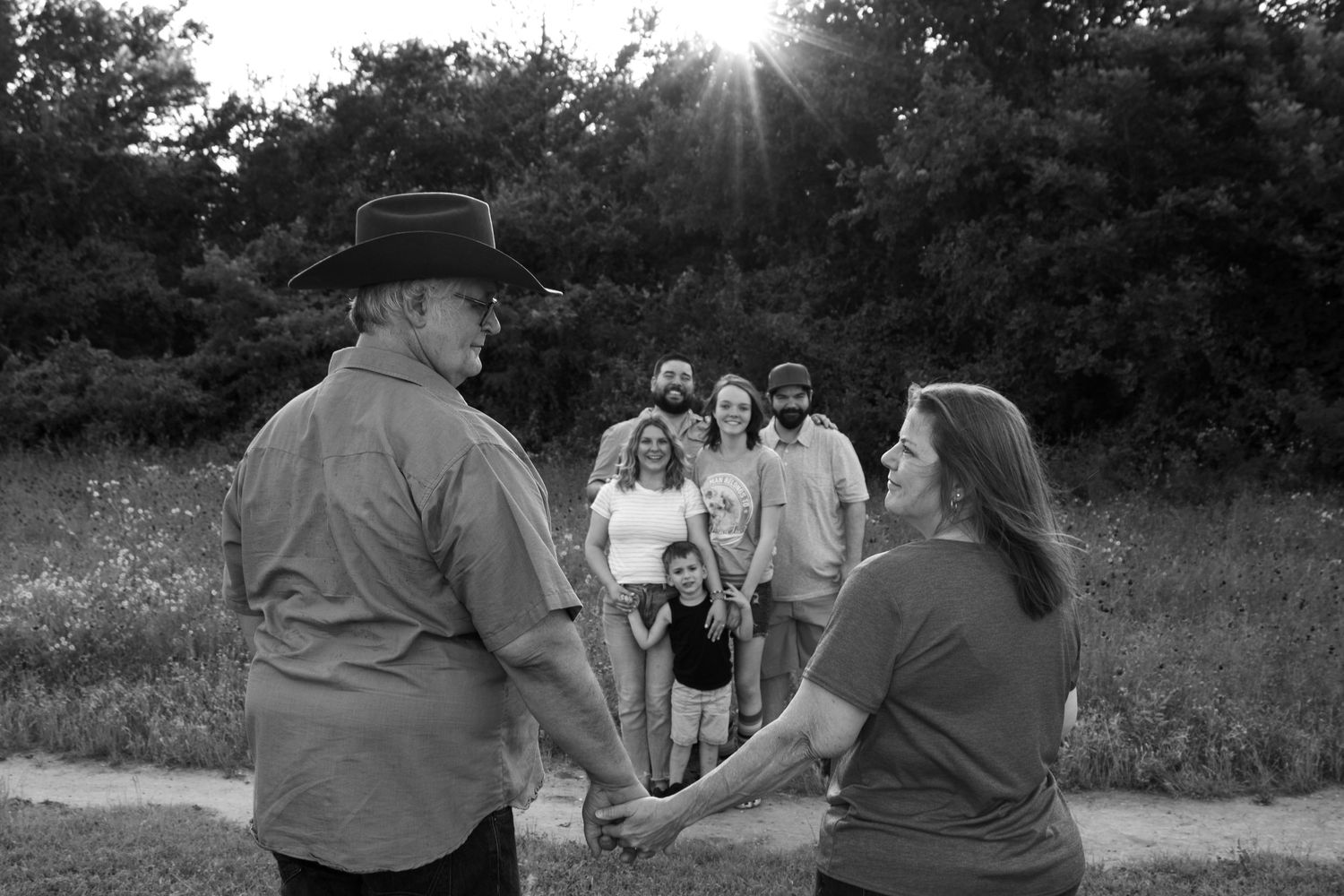 family in B&W with parents holding hands and family in background