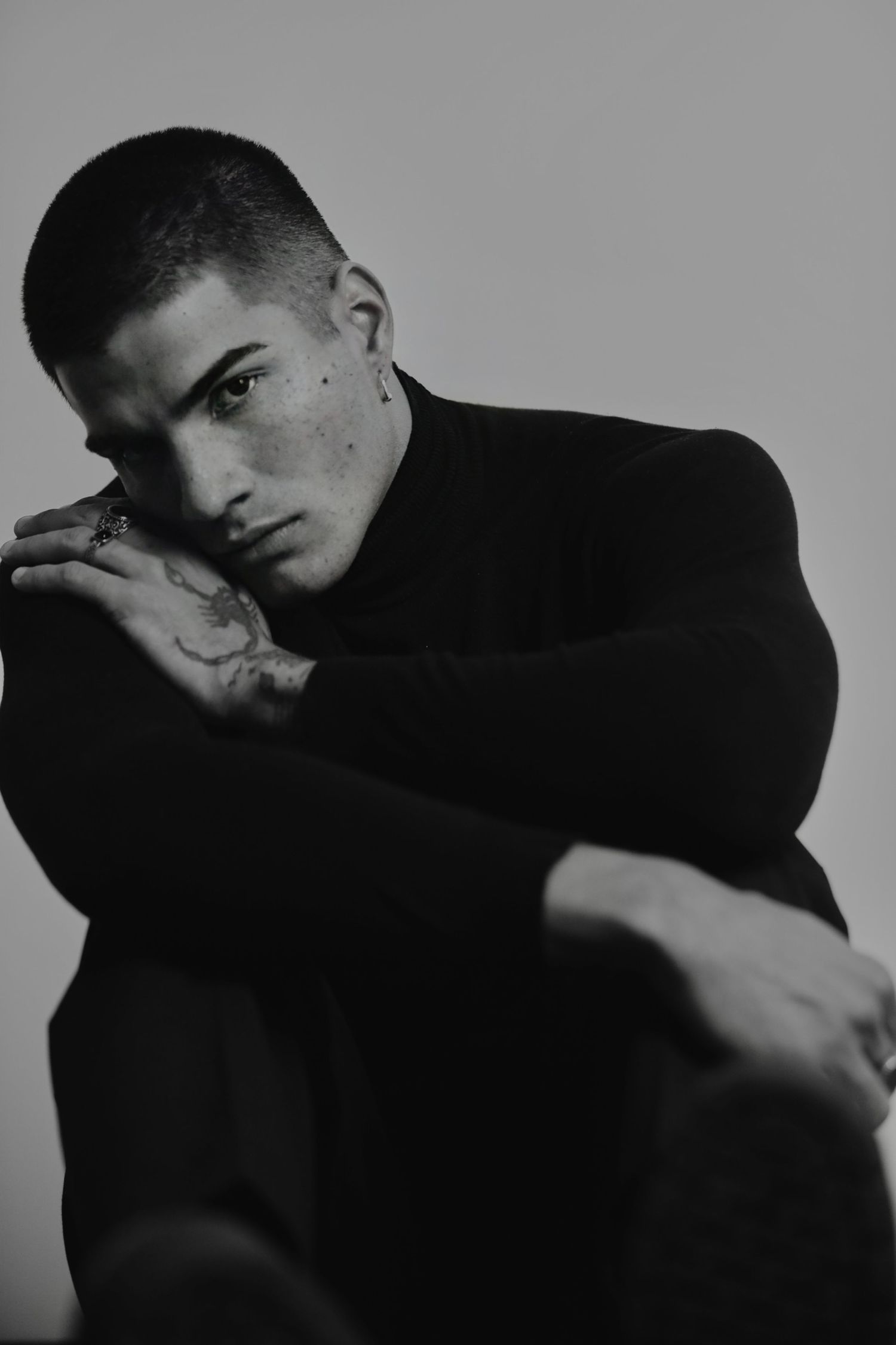 Black and white portrait of a man in dark clothing posing dramatically against a plain background.