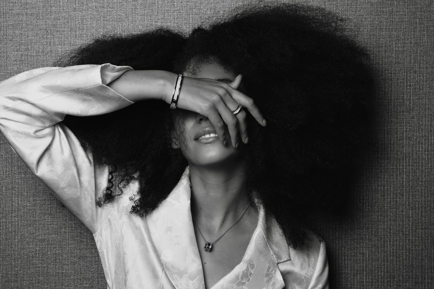 A black and white portrait of a laughing person with voluminous natural curly hair wearing a white shirt.