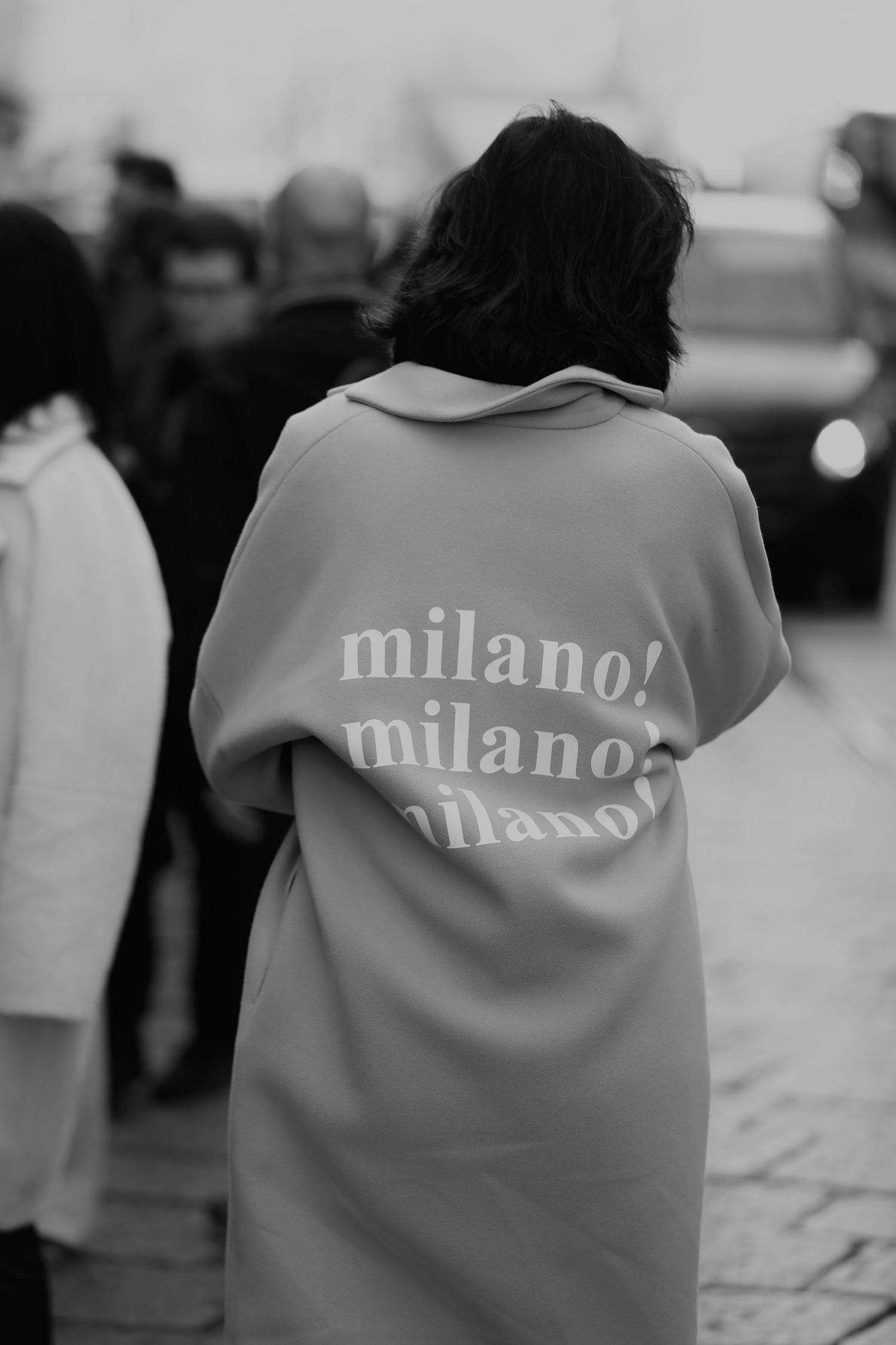 Black and white photo of a person wearing a white sweatshirt with 'milano' text repeated three times on the back.