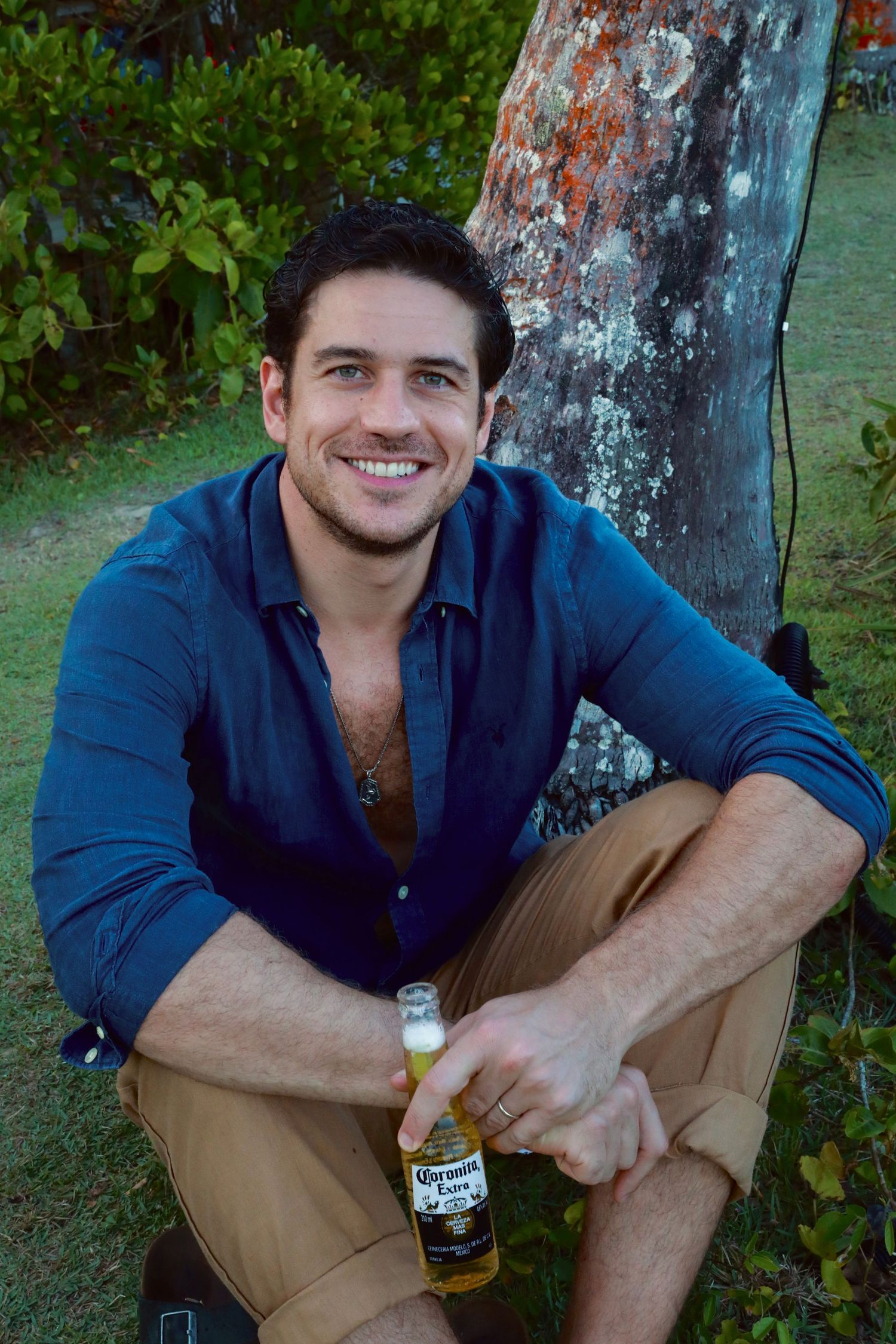 Casual portrait of man in blue shirt holding beer bottle while sitting outdoors.