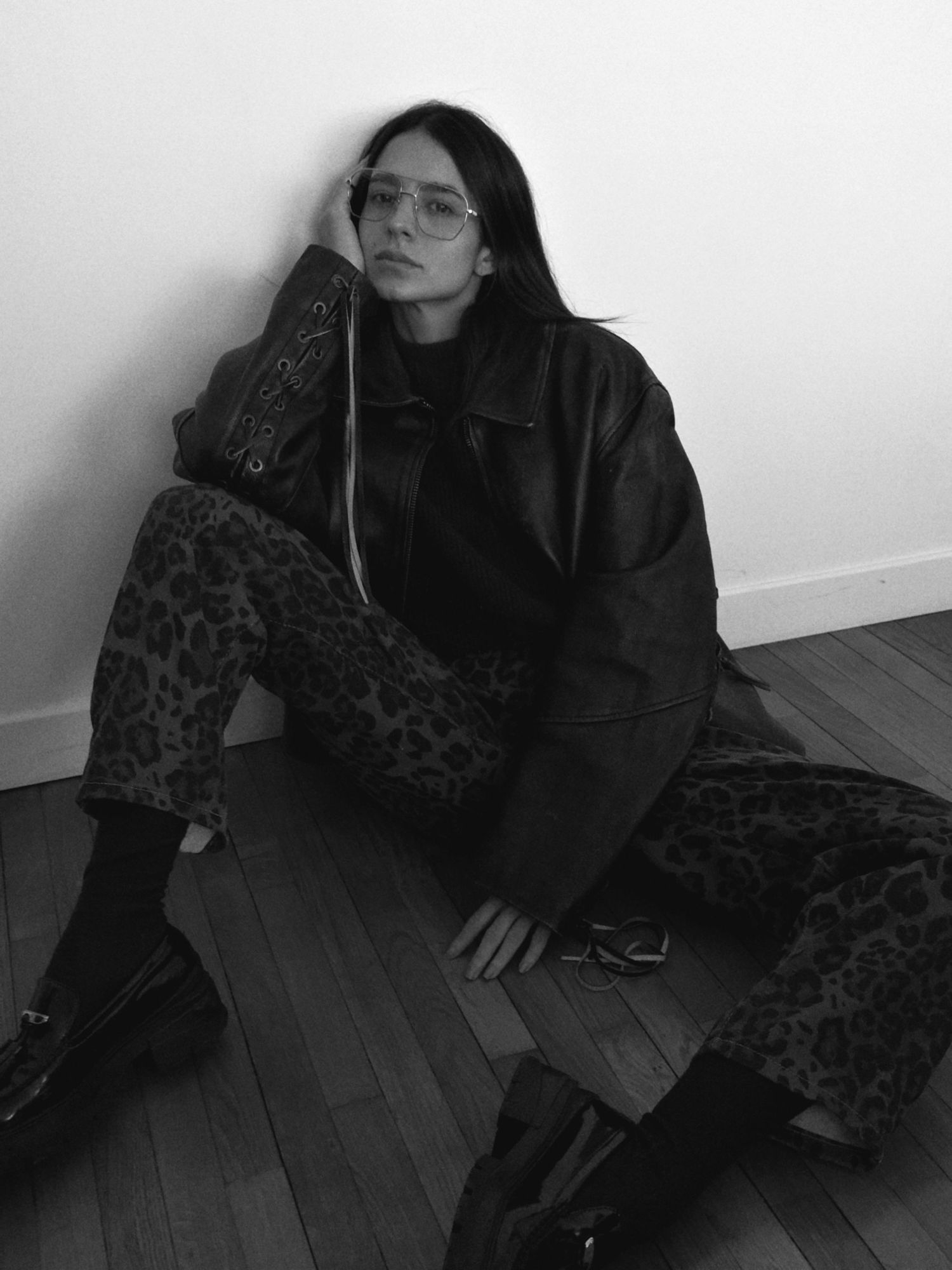 Black and white photo of person wearing glasses and leopard print pants on wooden floor.