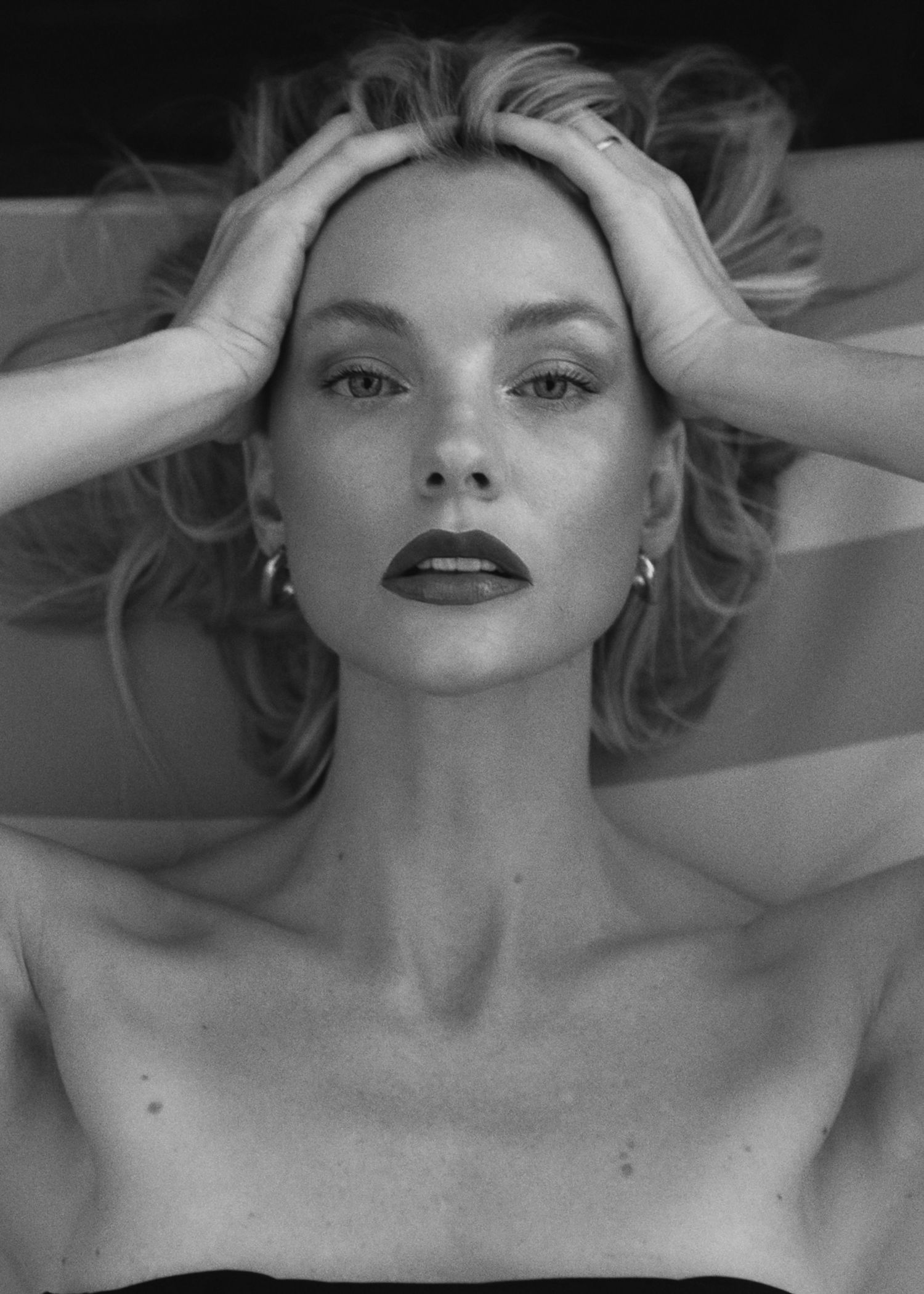Dramatic black and white portrait with hands framing face in artistic pose.