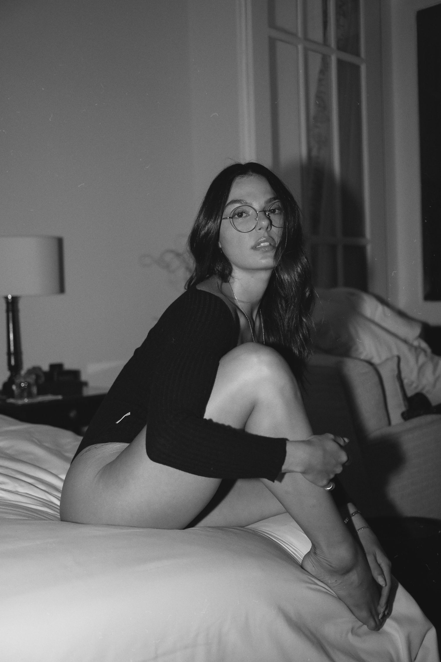 Black and white portrait of someone in a dark sweater lounging on a bed.