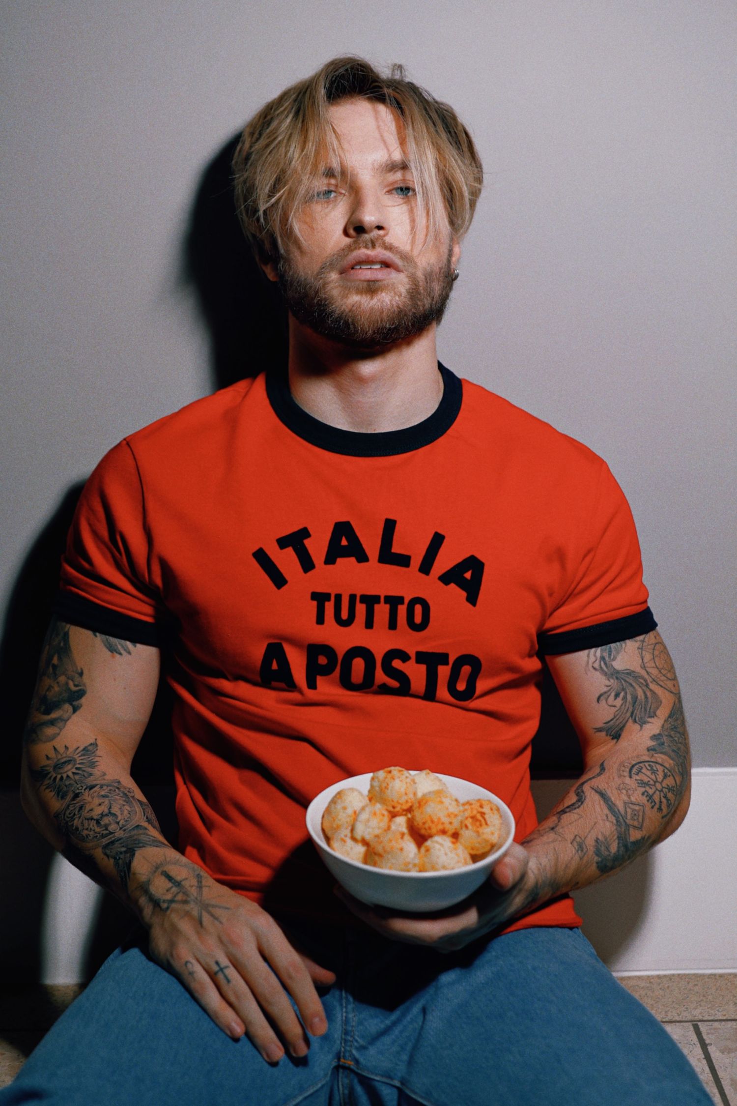 Man in orange Italia shirt holding bowl while posing against gray background.
