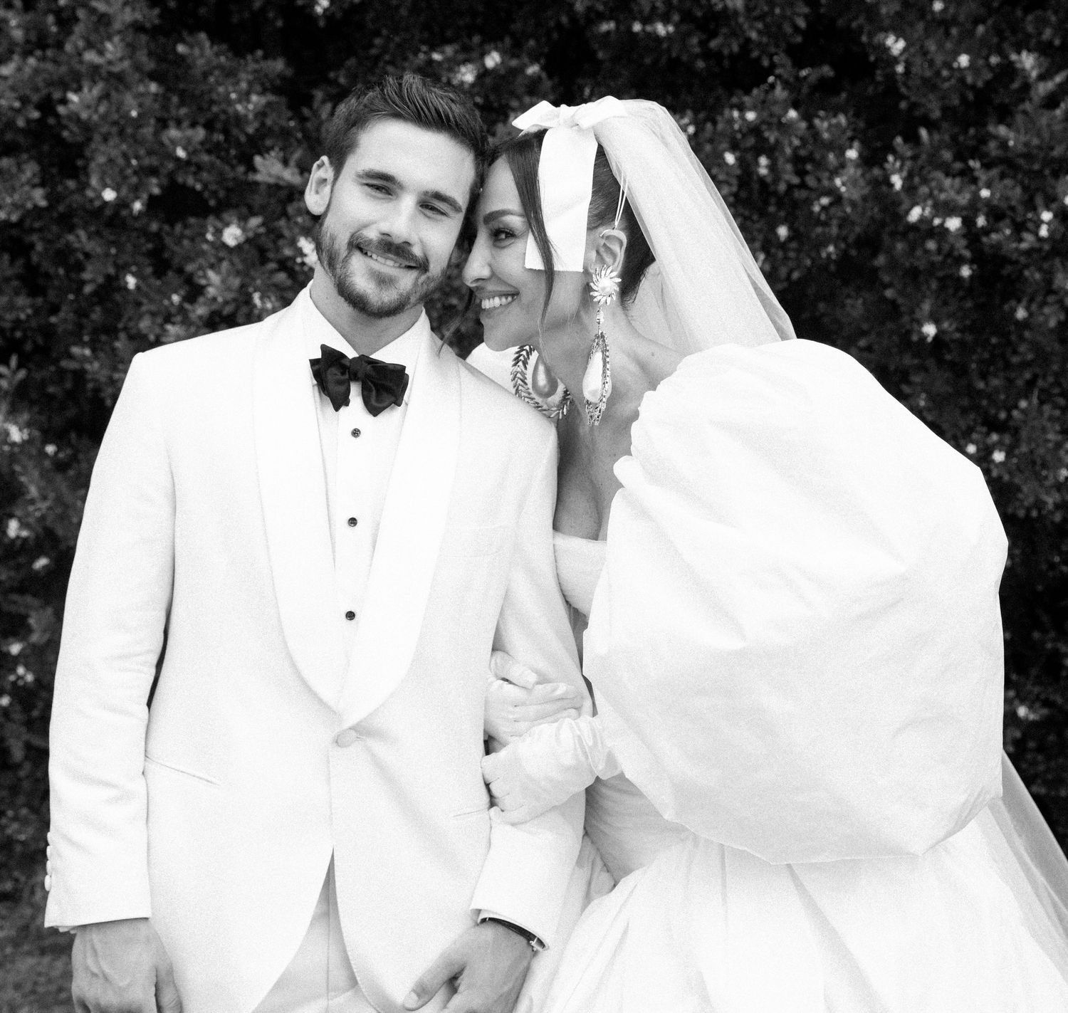 A black and white portrait of a bride and groom in white formal attire smiling together.