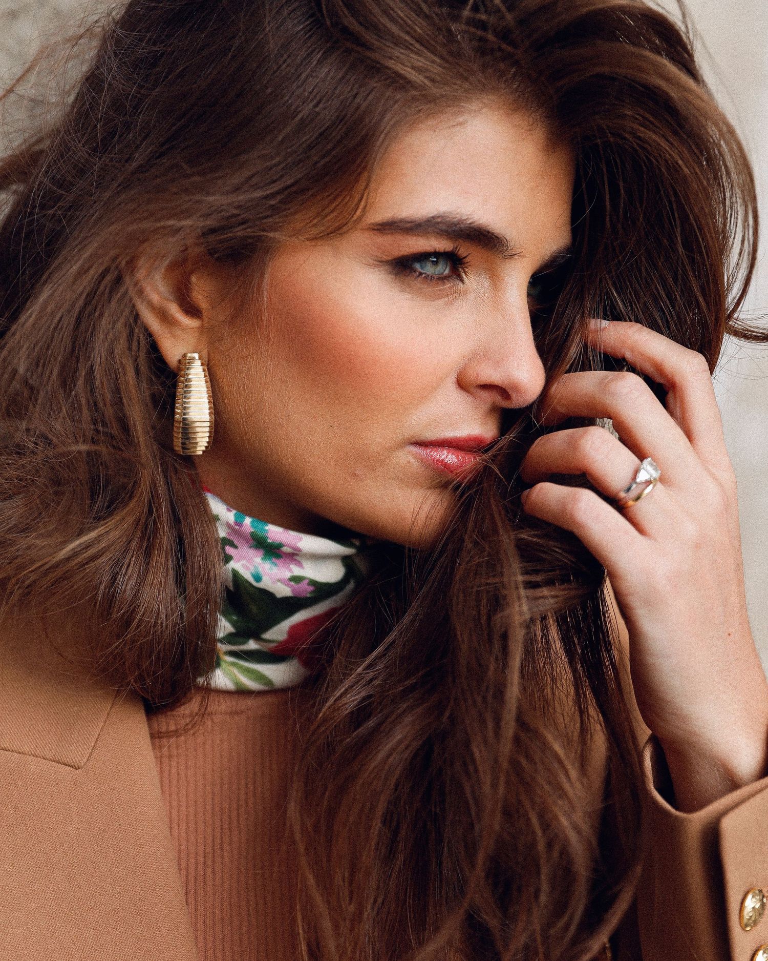 Portrait of woman in brown turtleneck with floral print showing statement earring and ring.