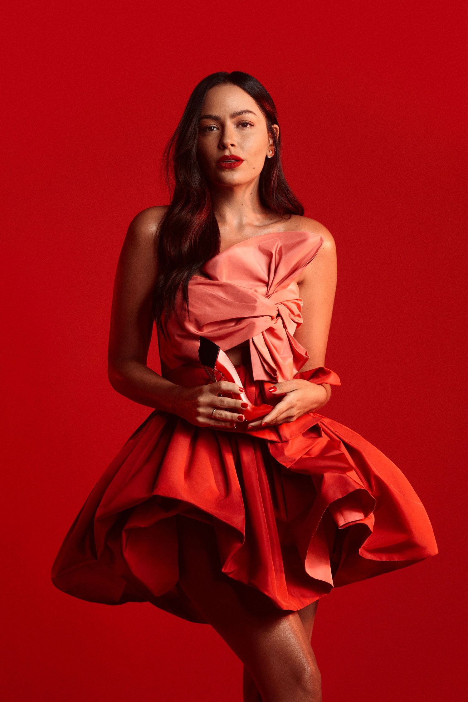 Short red cocktail dress with dramatic bow detail against vibrant red background.