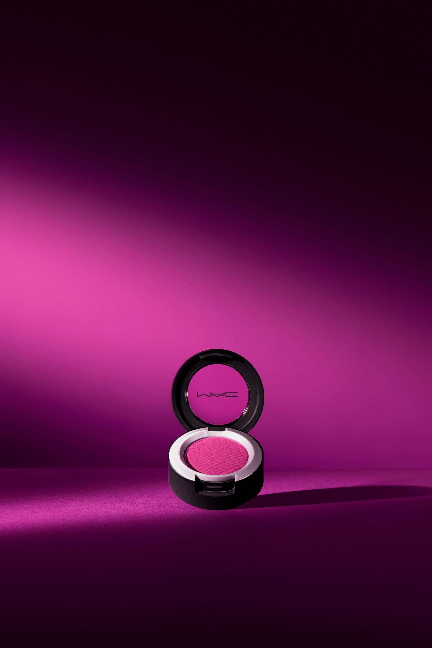 Pink MAC cosmetics powder compact isolated on purple gradient background.