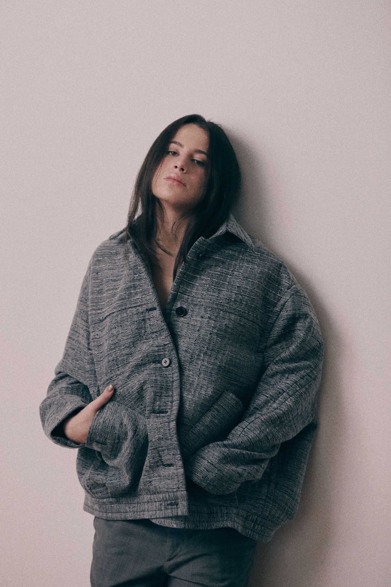 A person in an oversized gray textured jacket poses against a light background.